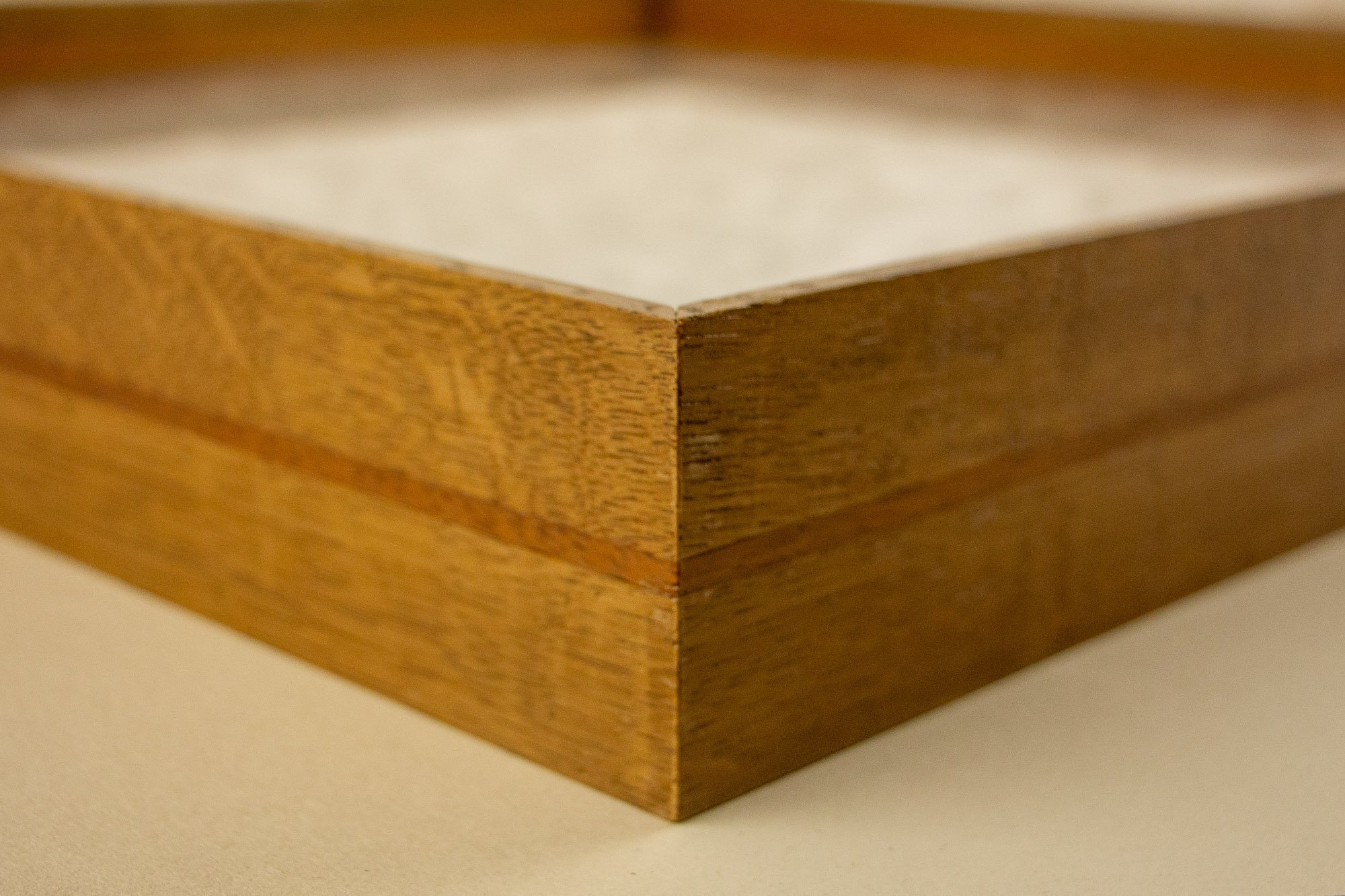 Veiled Alchemist 003 frame detail: corner close-up of the frame, showing the precise mitre, the warm Japanese elm exterior, and the fine reddish band running horizontally through the profile.