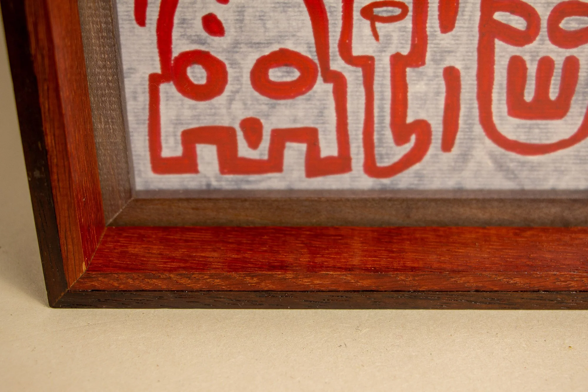 Unseen Signifiers 003 frame detail: lower-left inner corner view, showing the layered dark outer frame, the red inner lip, and the pale ground of the artwork with red linework behind the glass. mahogany, oak and beech wood.