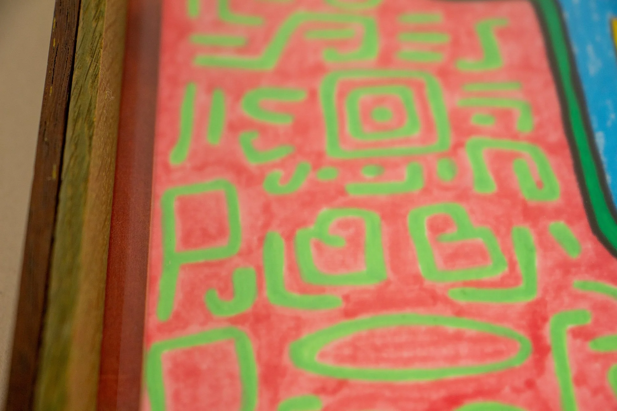 Unseen Signifiers 001 frame detail: close-up along the left inner edge of the frame, showing the olive-toned outer wood, the reddish inner liner, and the pink ground of the artwork with green sign-like forms. mahogany, oak and beech wood.