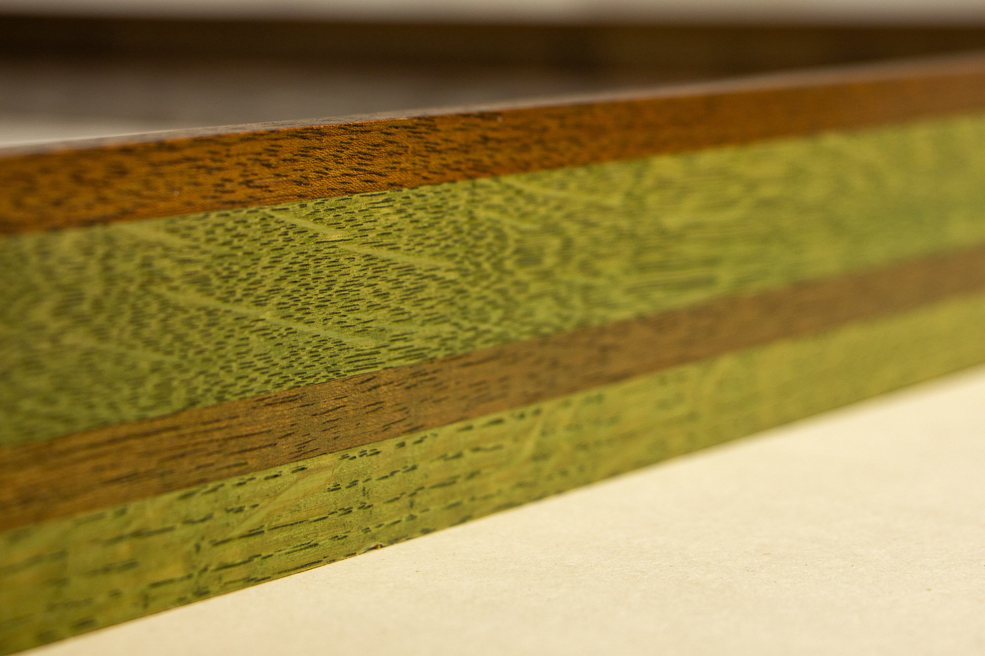 Resonant Syntax 004 frame: angled close-up of the frame side, emphasizing the layered construction, tonal rhythm, and the interplay of green, granada, and red across the oak and mahogany elements