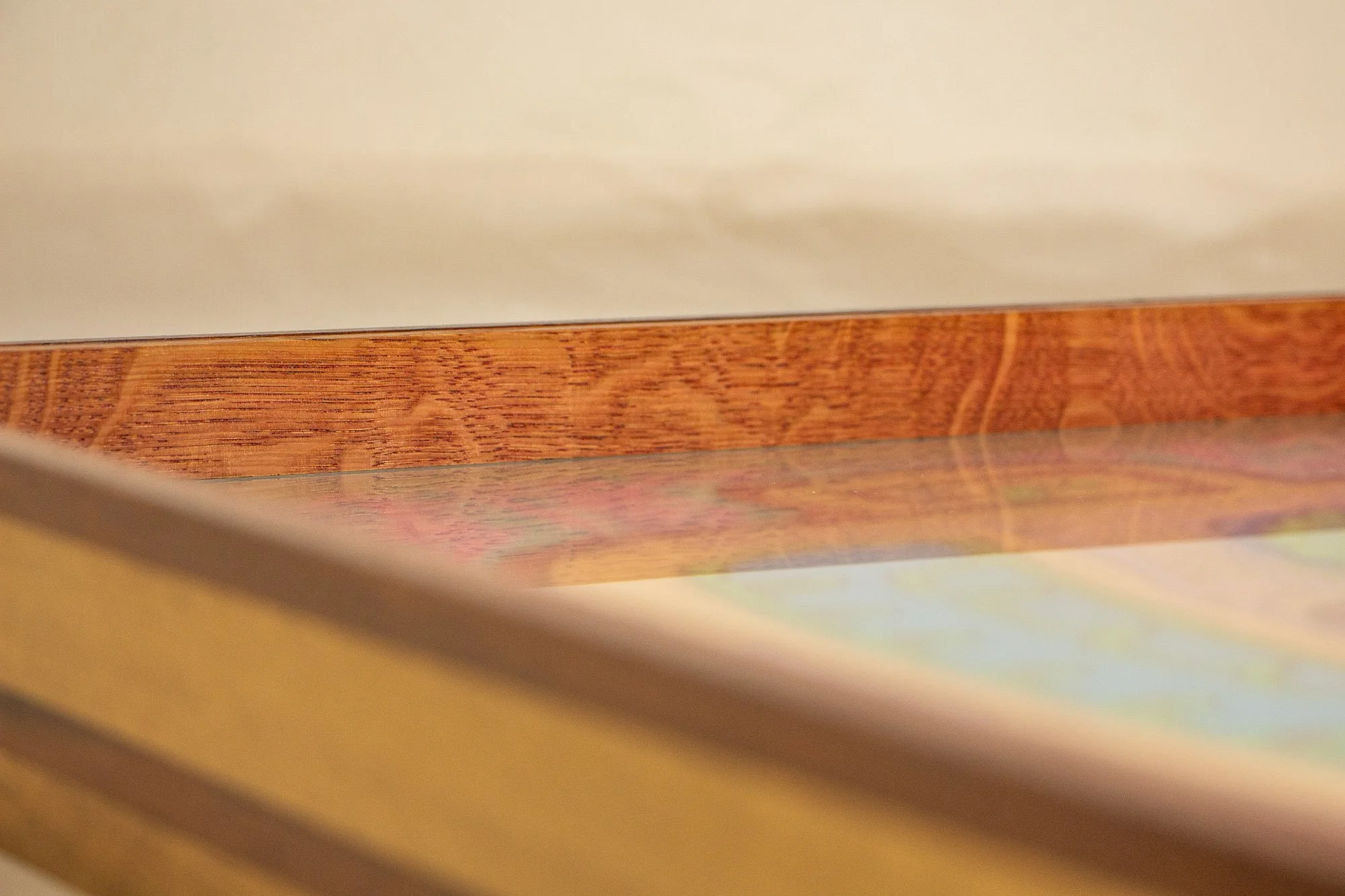 Unseen Signifiers 004 frame detail: low oblique close-up along the top interior edge, showing the warm reddish wood rail above the glazing with the artwork softly reflected beneath. mahogany, oak and beech wood.