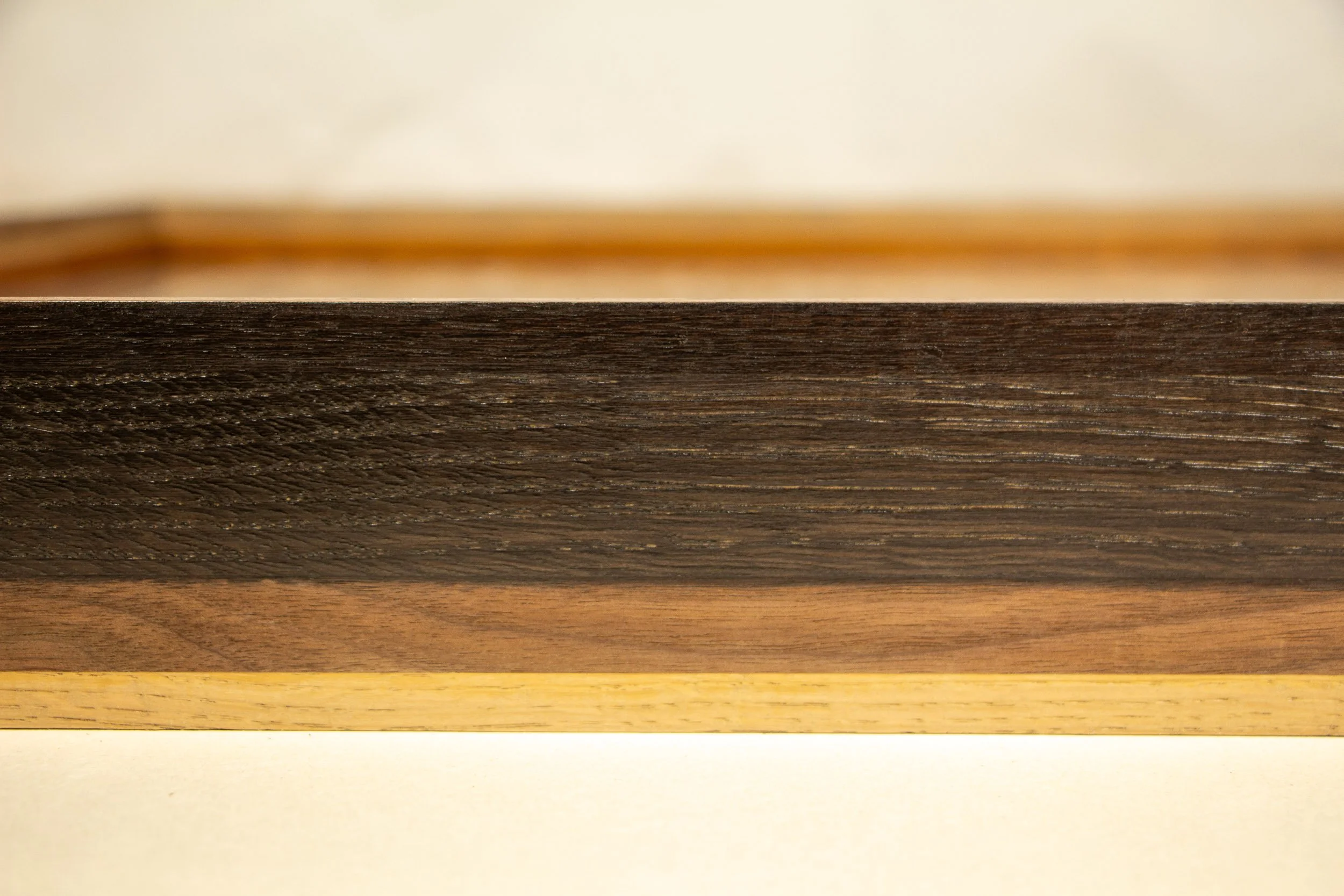 Mêlée of Discovery 004 frame: frontal side detail of the layered wood construction, with a broad dark band above warmer walnut and a thin oak line below.