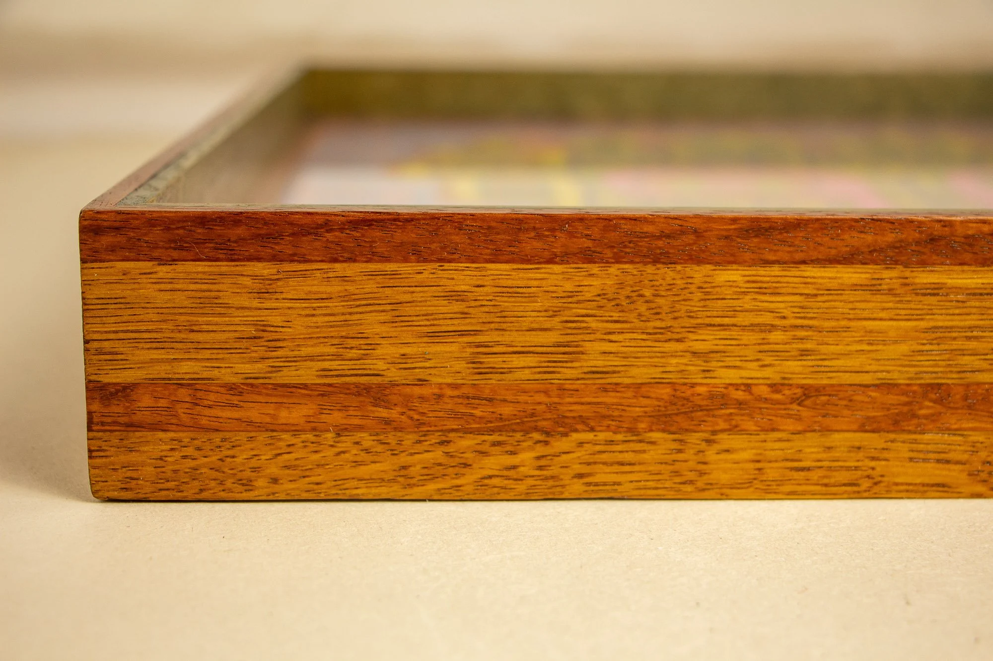 Unseen Signifiers 006 frame detail: angled close-up of the frame’s outer profile, showing the layered striped construction with a narrow reddish-brown top band above a broader golden wood band. mahogany, oak and beech wood.