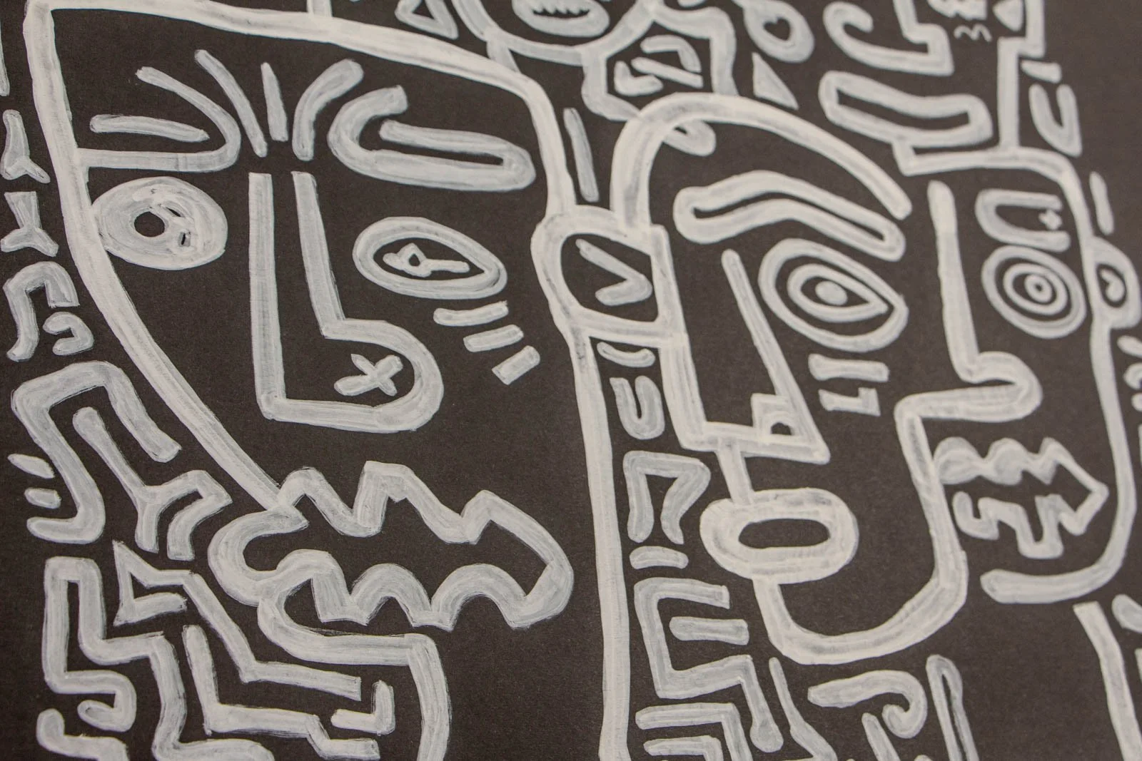 Metamorphic Entwining 002 detail: furrowed-brow profile with L-shaped nose marked with an X, paired with a second face, jagged cloud mouth motif, white ink on black paper