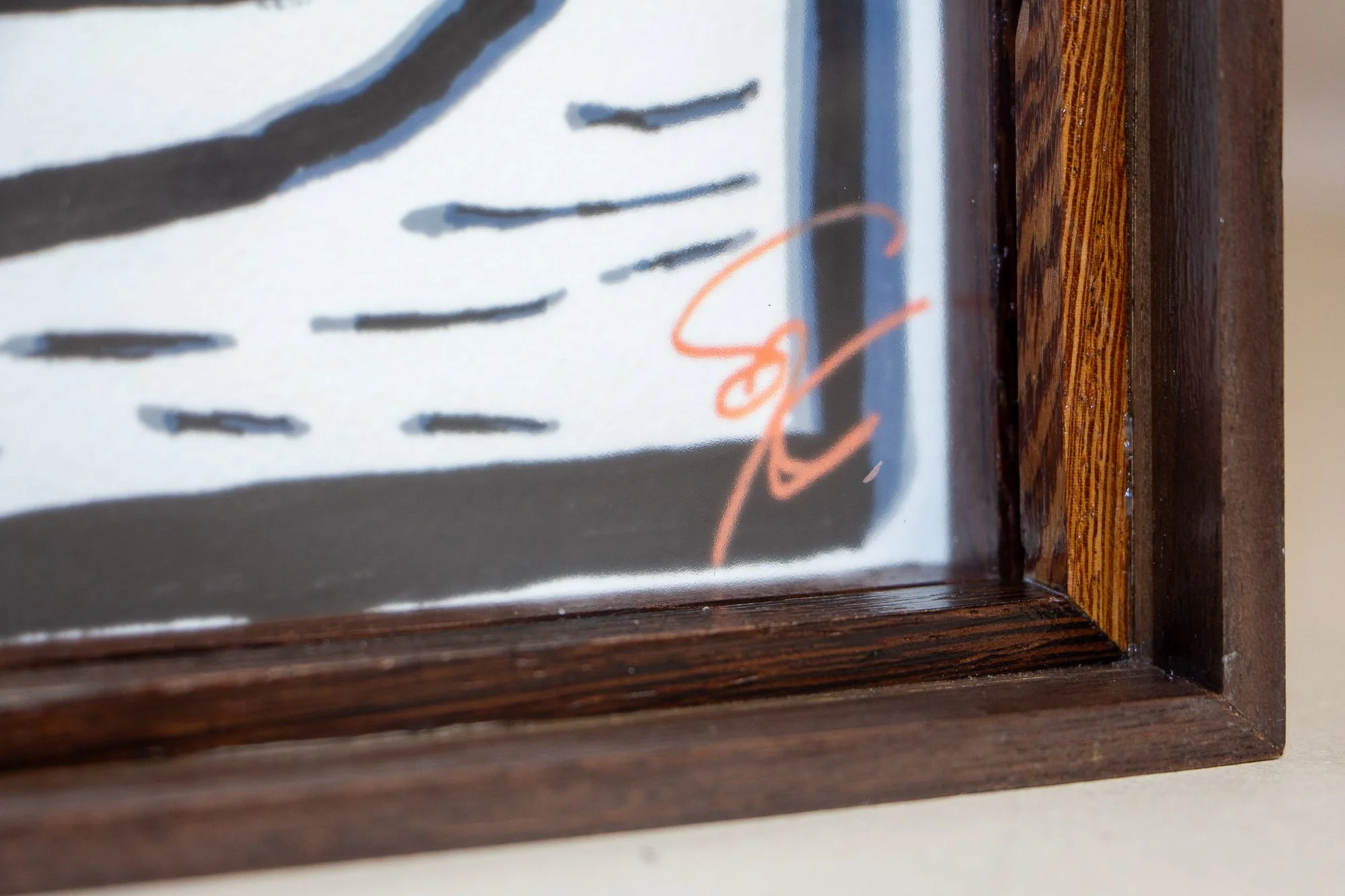 Luminous Parallax 002 frame: lower corner detail of the glazed artwork, showing the artist’s signature in soft coral near the edge and the dark inner frame surrounding it.