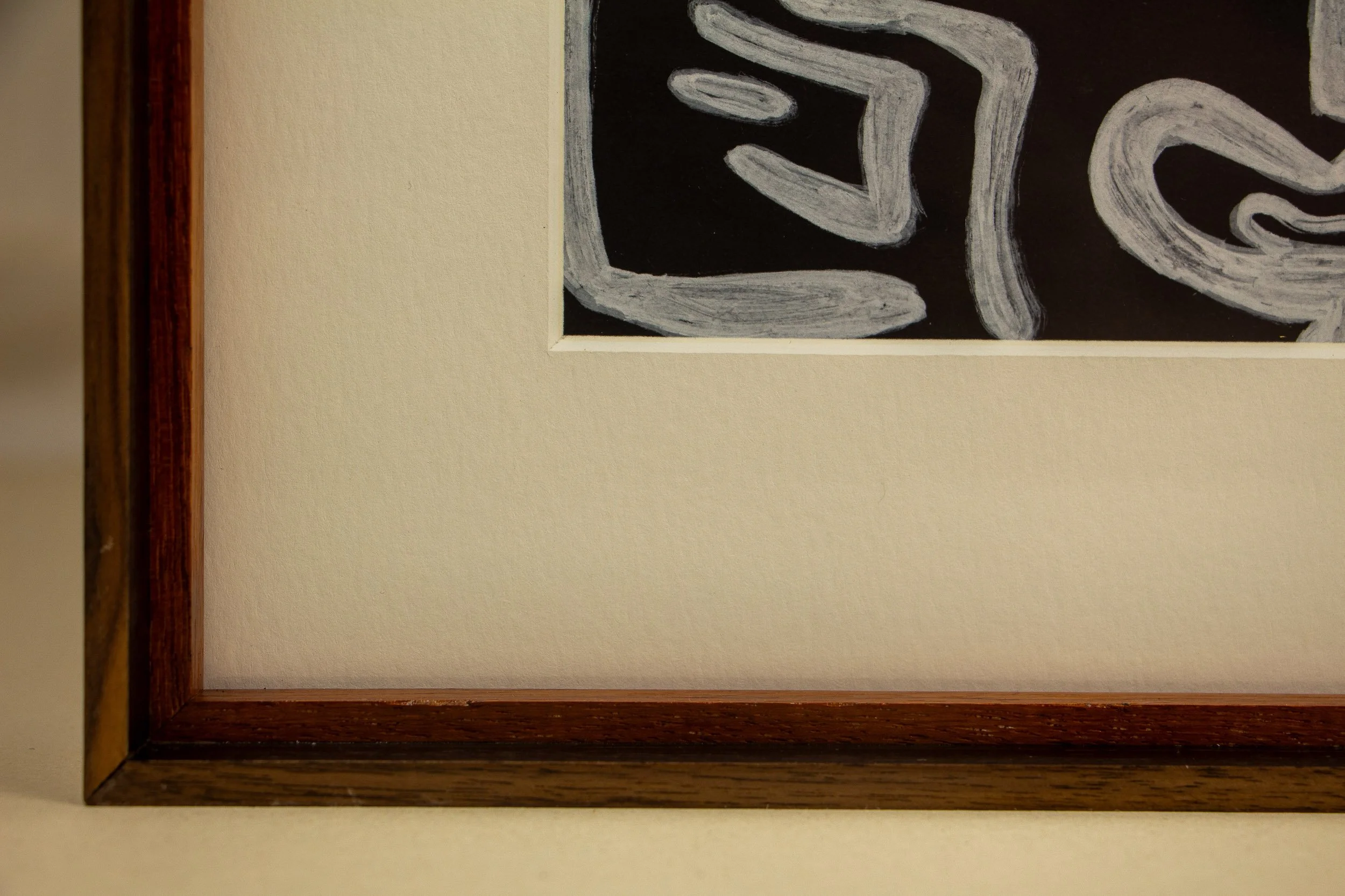 Close-up photo of a framed piece of artwork with black background and white abstract lines, hung on a beige wall.