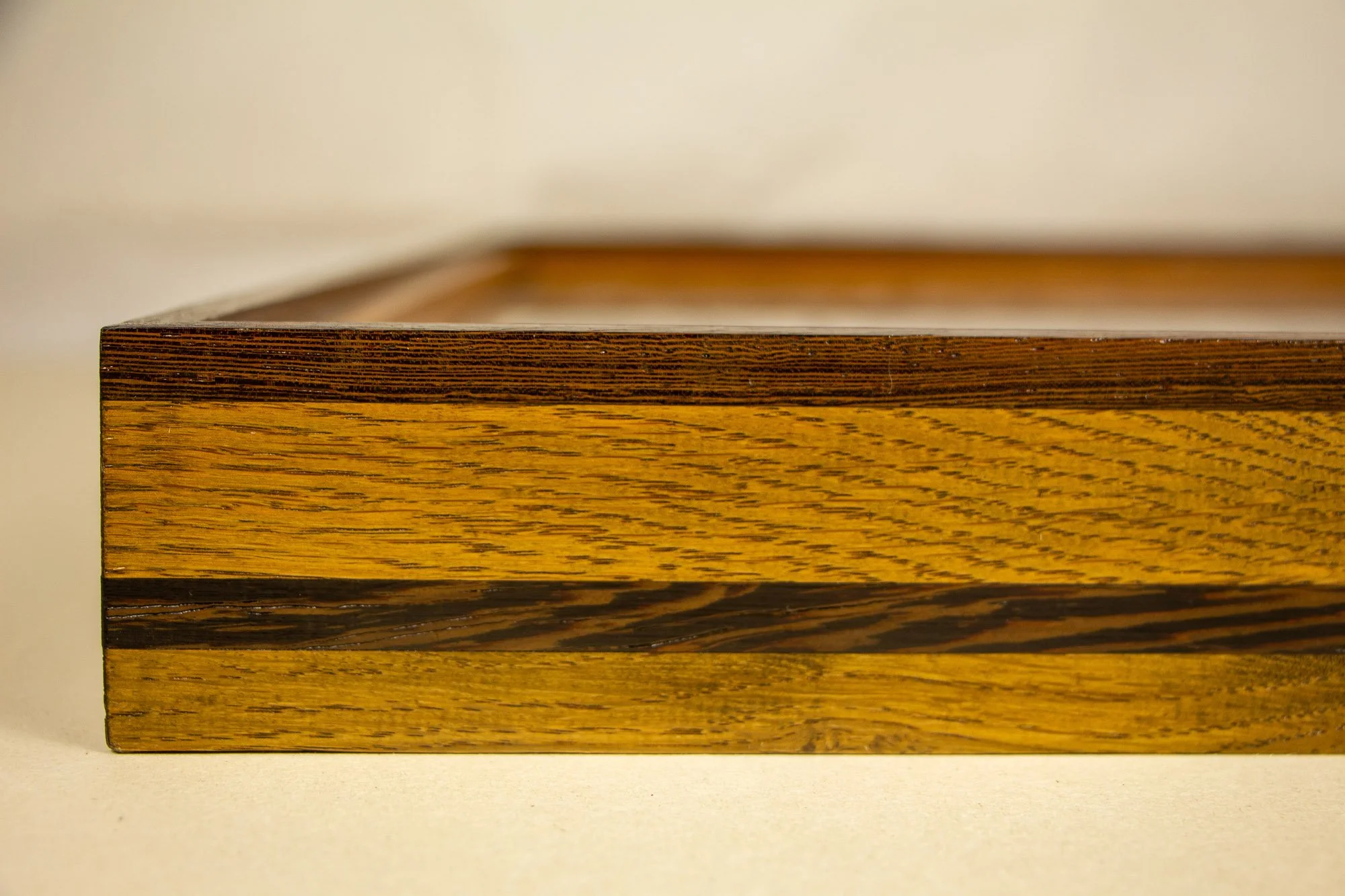 Elusive Cocoon 002 frame: angled side view of the frame construction, showing the shallow dark upper rail, golden oak-toned body, darker figured central strip, and elongated low-profile depth.