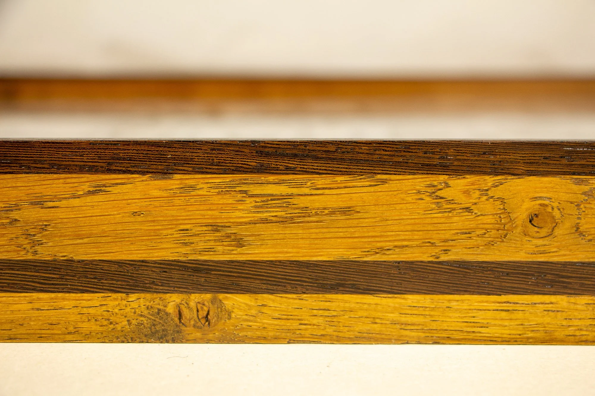 Elusive Cocoon 002 frame: frontal close-up of the layered frame profile with a dark upper rail, broad golden oak-toned band, darker figured diagonal strip, and visible knots and grain variation across the wood.