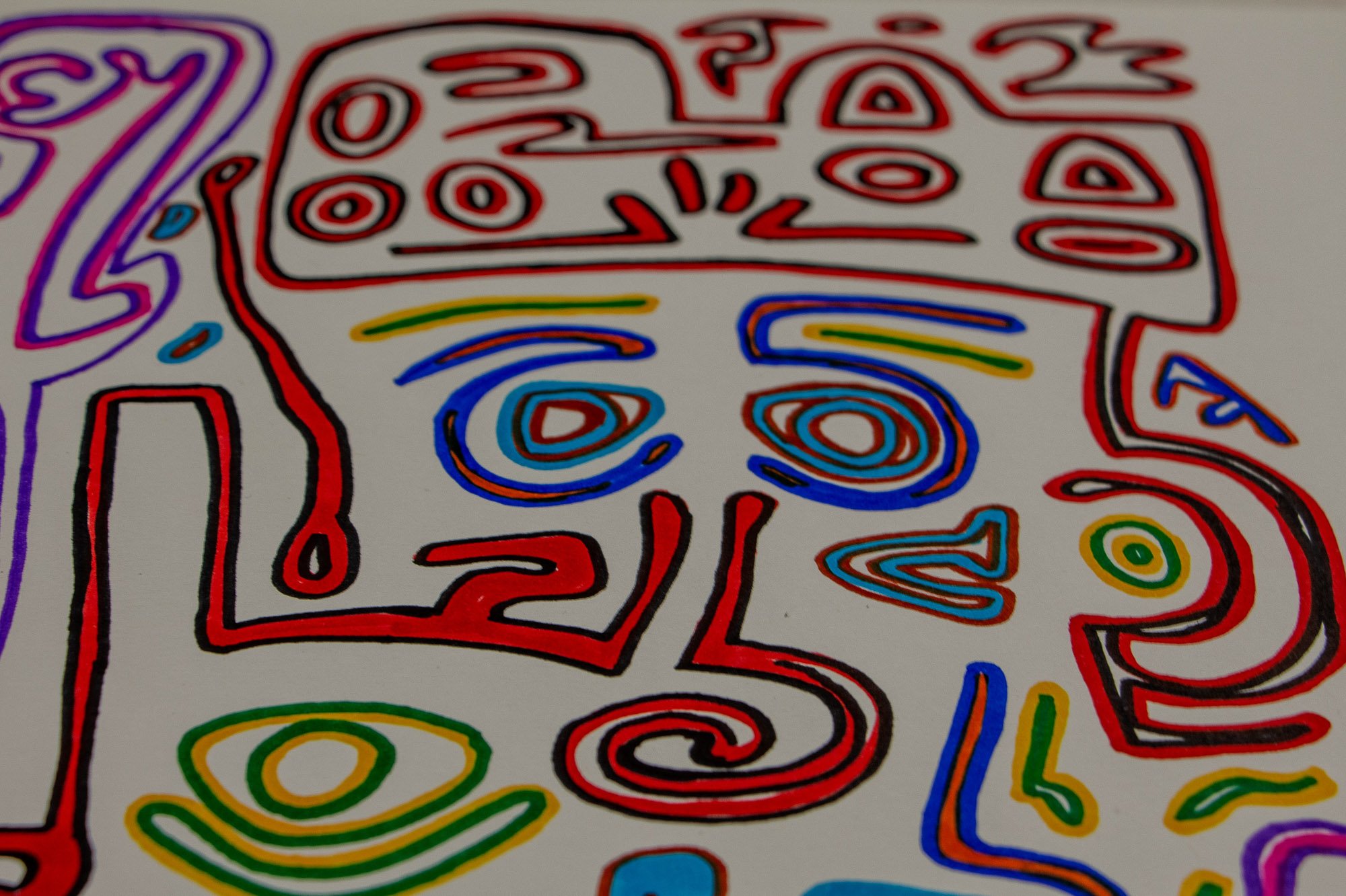 Eclipsing Gravitas 003 detail: frontal view of a red-outlined face-like figure with blue concentric eyes, a spiral lower contour, and crown-like symbols above, set among green, yellow, and violet elements across the white surface.