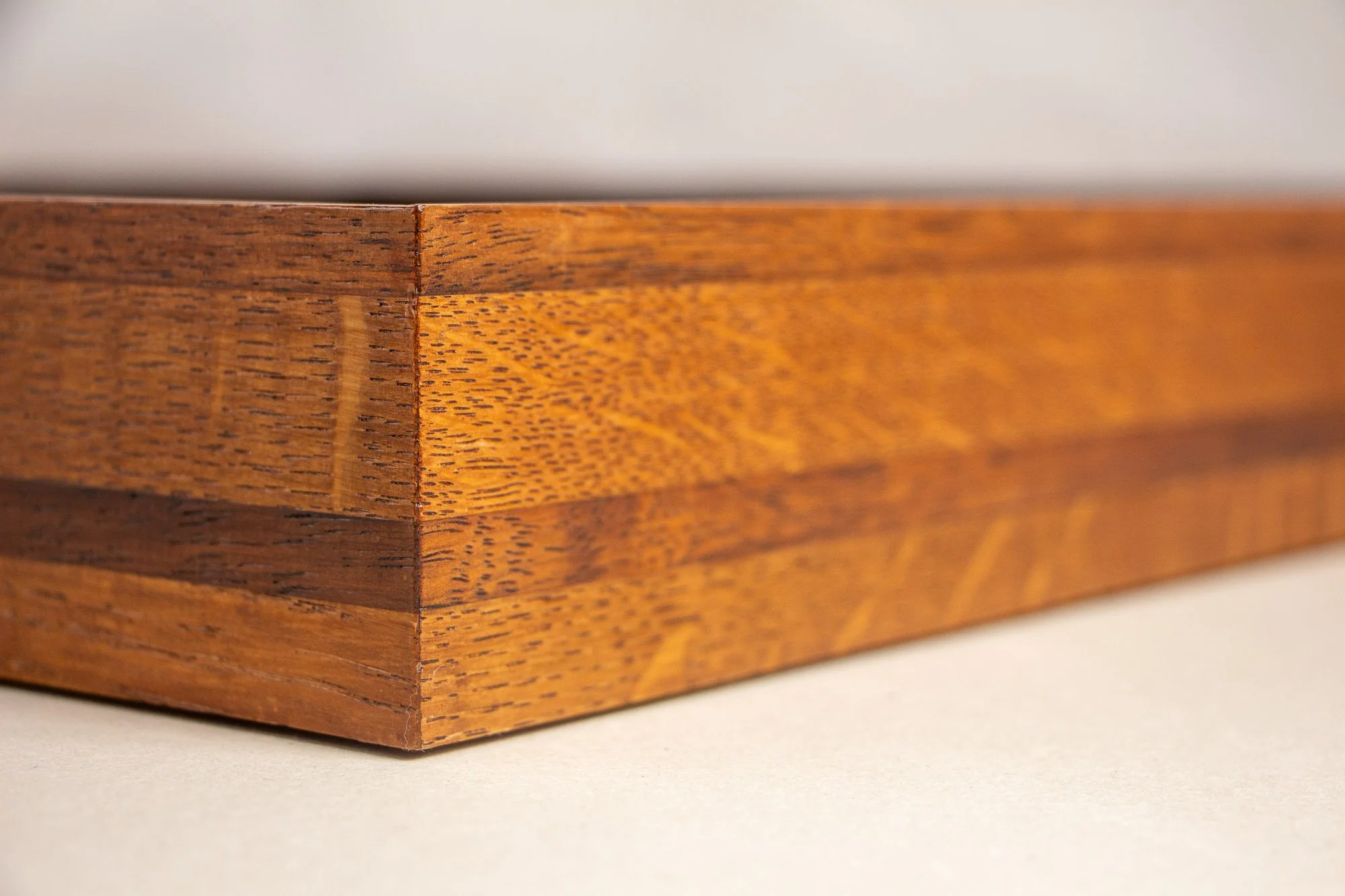 Turbulent Aegis 002 frame detail: angled corner close-up of the handcrafted frame, showing the precise join, warm lacquered wood grain, and the layered tonal structure of the frame body.