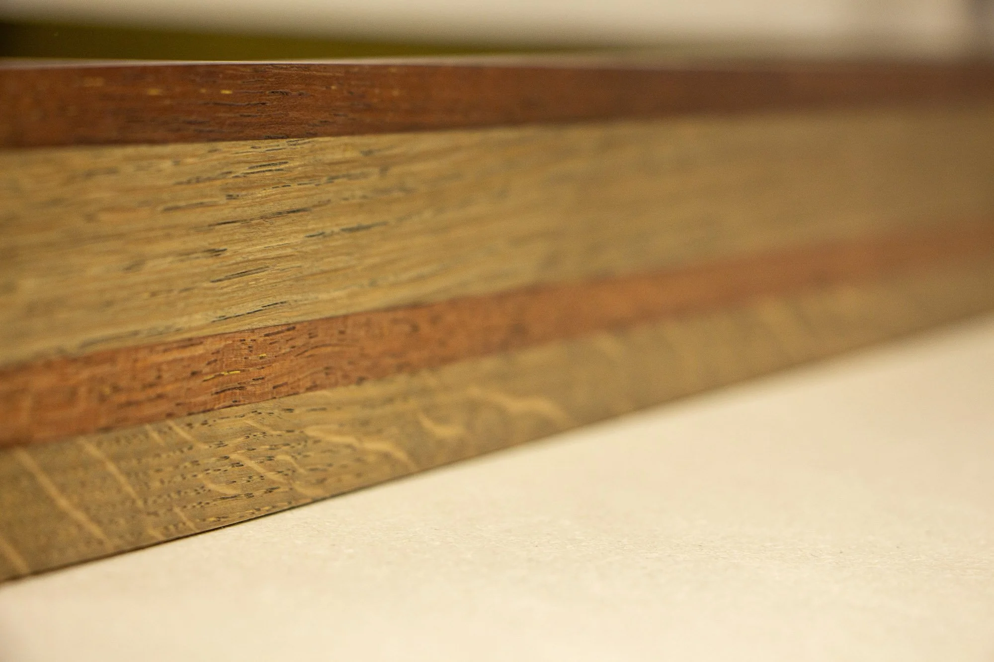 Unseen Signifiers 001 frame detail: oblique close-up of the frame side, showing the polished reddish upper edge, the lighter oak band beneath it, and the darker strip running through the centre. mahogany, oak and beech wood. mahogany, oak and beech w