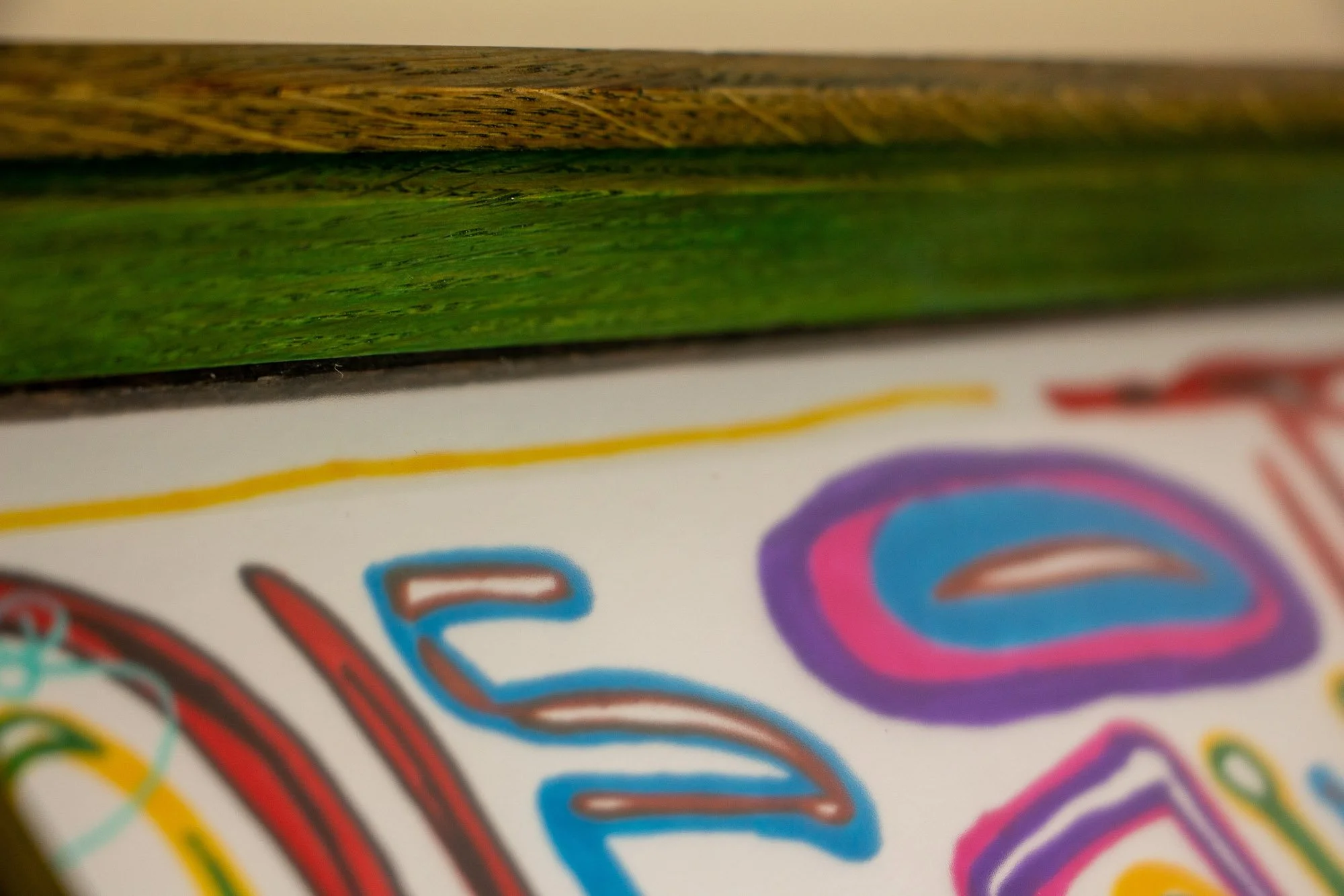 Eclipsing Gravitas 002 frame: side macro of the shallow frame profile, highlighting the olive-green toned oak, the vivid green inner lip, subtle grain variation, and softly blurred linear forms of the drawing under glass.