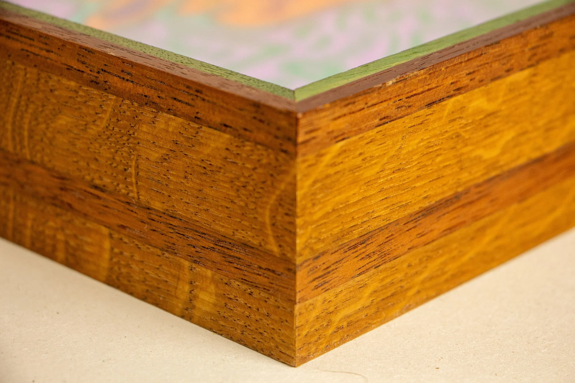 Close-up of a corner of a wooden picture frame with visible wood grain and a green mat inside.