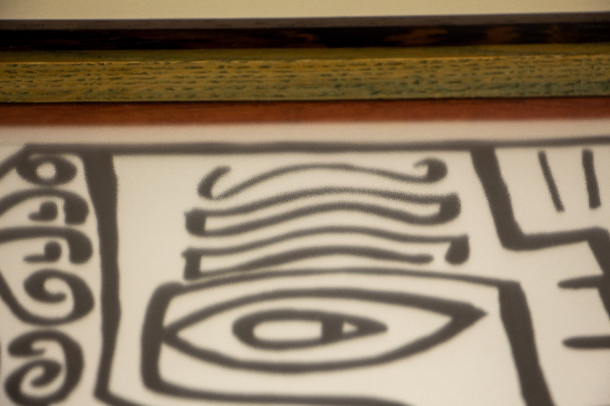 Elusive Cocoon 004 frame: upper-edge detail with a dark wengé outer rail, olive-toned inner band, and a warm orange inner lip bordering the black line drawing beneath the glass.