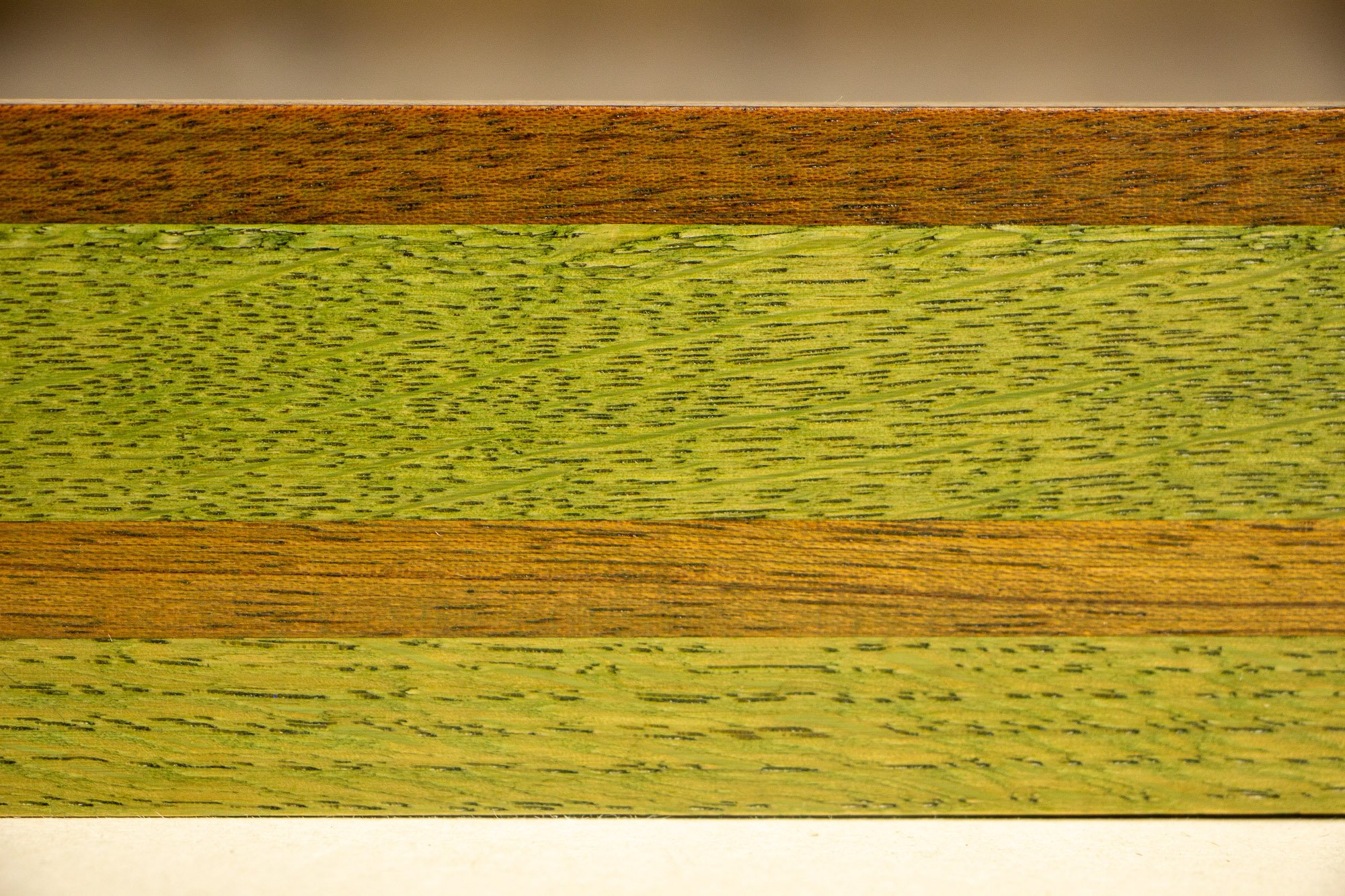 Resonant Syntax 004 frame: horizontal close-up of the frame profile, showing layered green, granada, and red-toned bands with pronounced grain variation and a refined satin finish