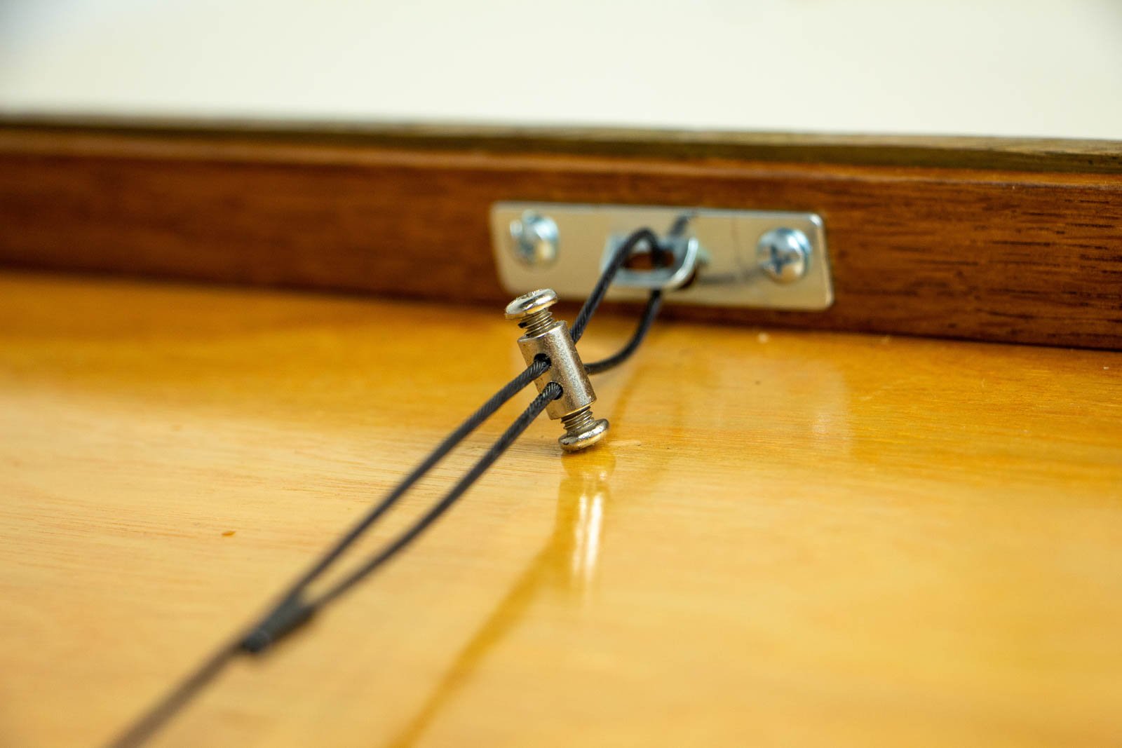 Metamorphic Entwining 004 frame: macro of the hanging system, nylon-coated twin wire joined by a nickel barrel coupler, secured to a steel plate with cross-head screws on the top rail; clean, stable install