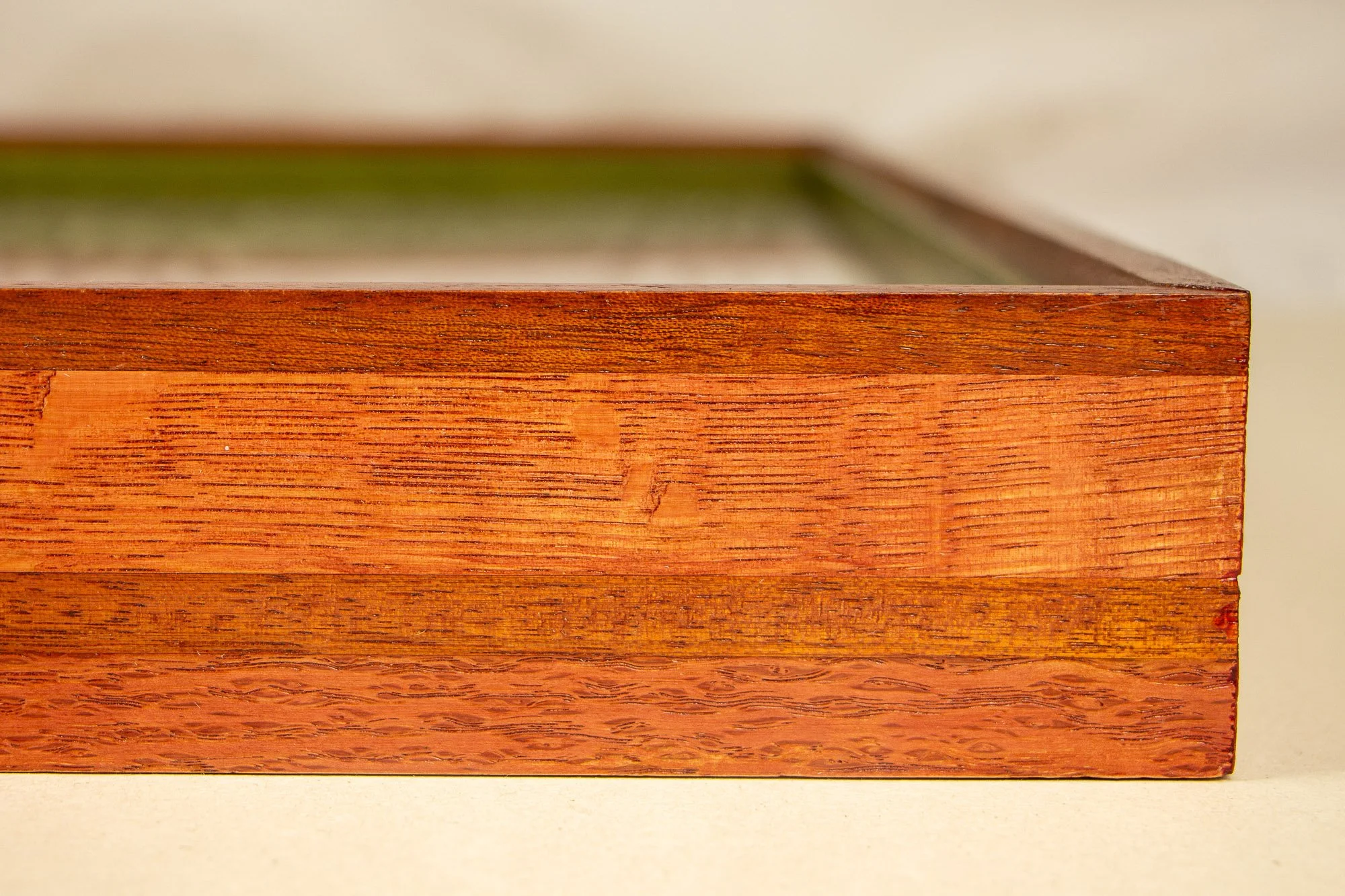 Resonant Syntax 003 frame: horizontal close-up of the frame profile, with a layered red, granada, and red-toned construction, pronounced grain variation, and a smooth satin finish across the wood surface