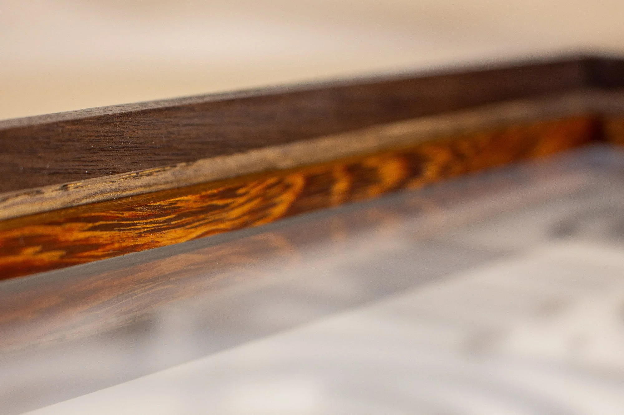 Luminous Parallax 001 frame: angled corner detail of the frame interior, showing precise mitered joinery, a dark exterior profile, and a richly striped inner wooden recess around the glazing.