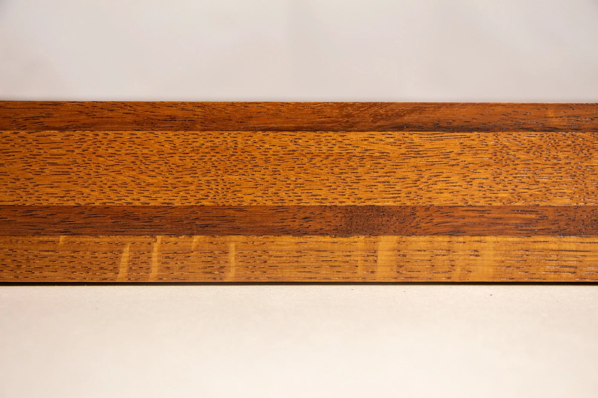 Turbulent Aegis 002 frame detail: frontal side view of the handcrafted frame, highlighting the horizontal grain, tonal banding, and warm amber-brown finish across the layered wood surface.