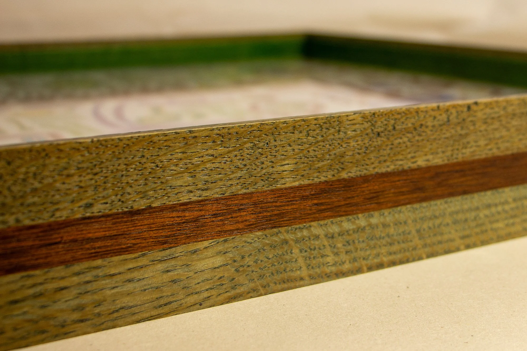 Eclipsing Gravitas 002 frame: macro side detail of the layered oak-and-mahogany construction, highlighting olive-green toned oak, a warm mahogany band, visible grain texture, and the green inner rim softly receding in the background.