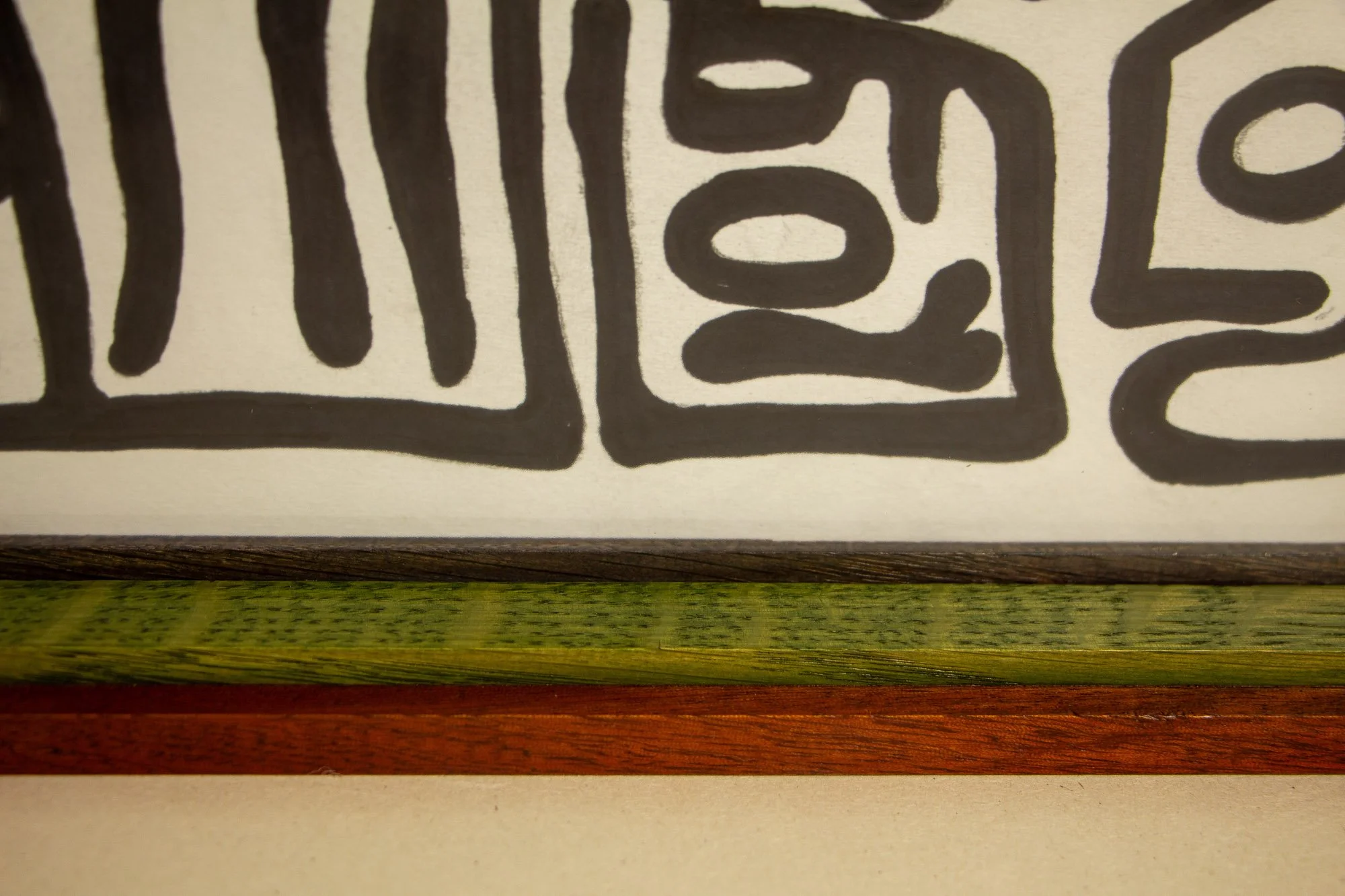 Resonant Syntax 003 frame: lower-right corner detail showing the green signature on paper, bordered by the granada inner lip, green spacer, and red outer frame