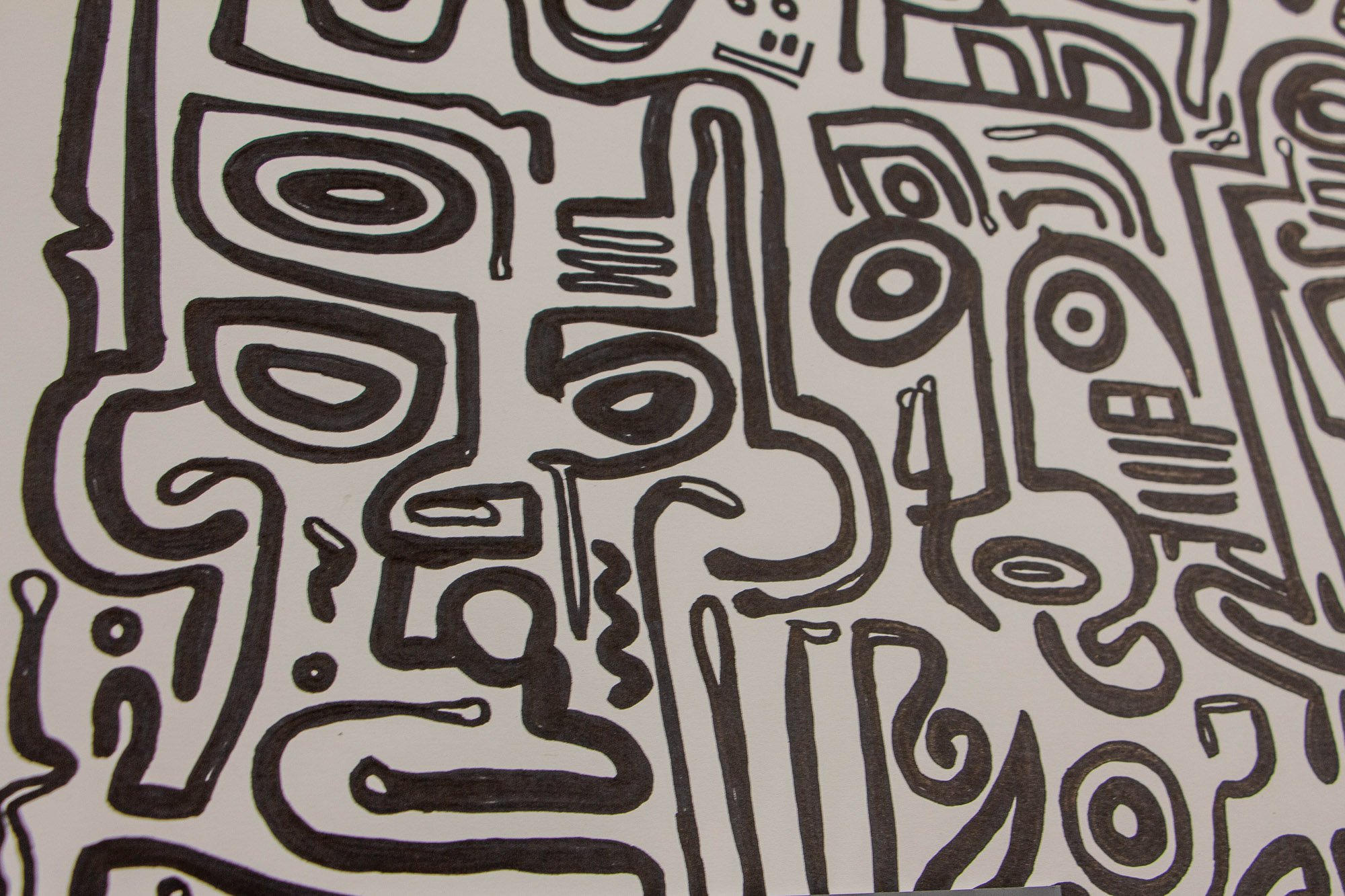 Veiled Alchemist 001 detail: close-up of interlocking black line faces and symbols on white paper, showing the dense layered composition, shifting expressions, and the tension between profile, eye, and contour.
