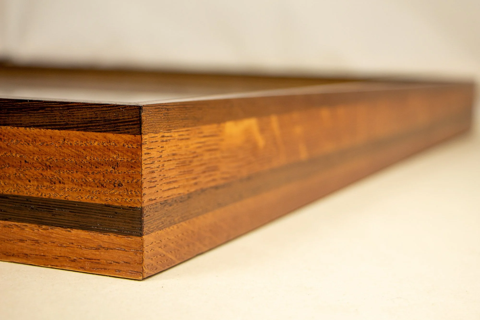 Elusive Cocoon 001 frame: close-up of the mitered front corner of the layered wooden frame, with aligned grain, a dark palisander edge, and a warm ash-toned band extending along the side.