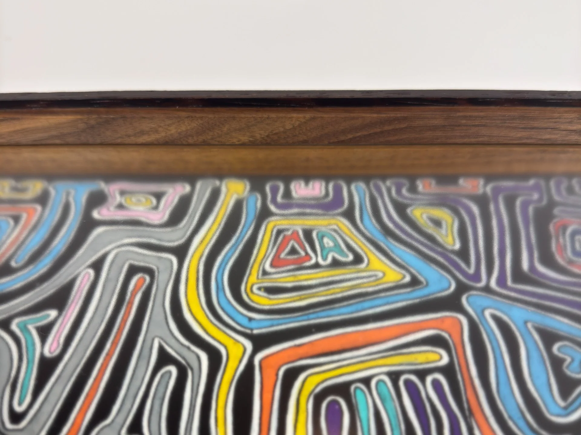 Close-up of the upper frame edge, focusing on the smooth wood grain, darkened outer band, and inner walnut lip, with abstract colored forms from the composition softly visible below.