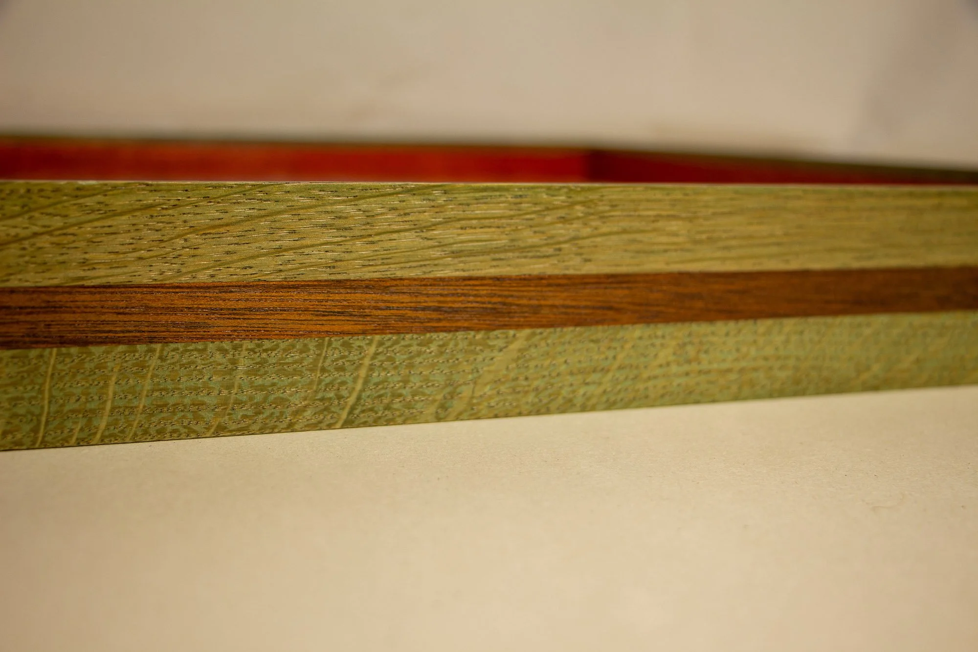 Eclipsing Gravitas 001 frame: frontal side detail of the layered oak-and-mahogany construction, with green-toned oak bands, a warm central mahogany strip, and visible natural grain variation.