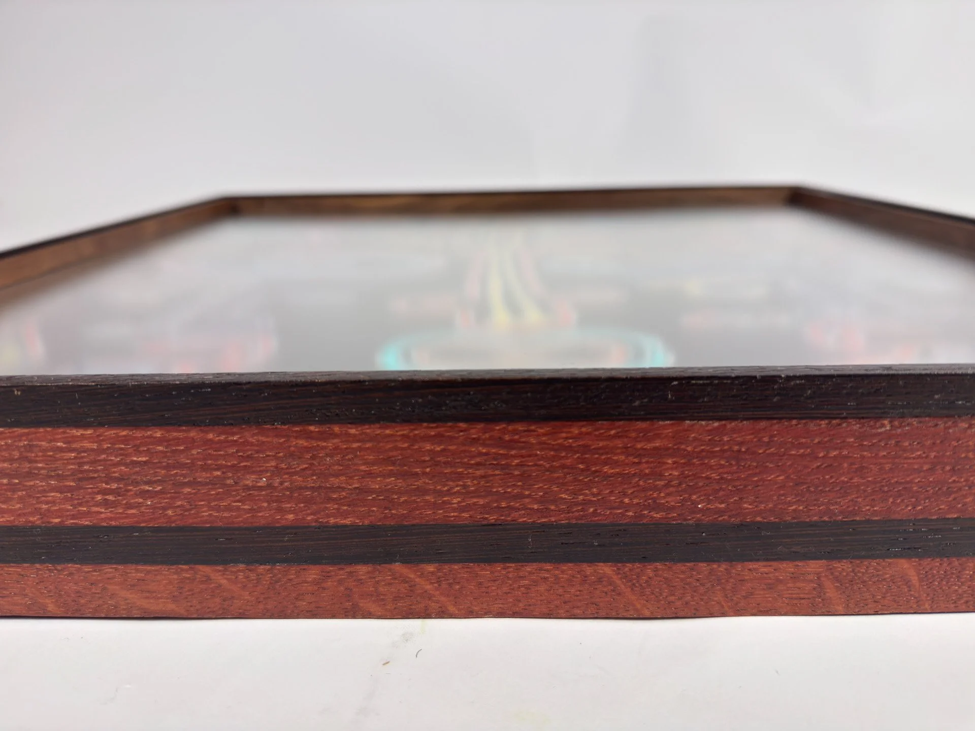 Frontal low-profile view of the frame, emphasizing its horizontal depth, layered wood construction in wengé, oak, and walnut, and the softly visible face composition receding behind the glazed surface.