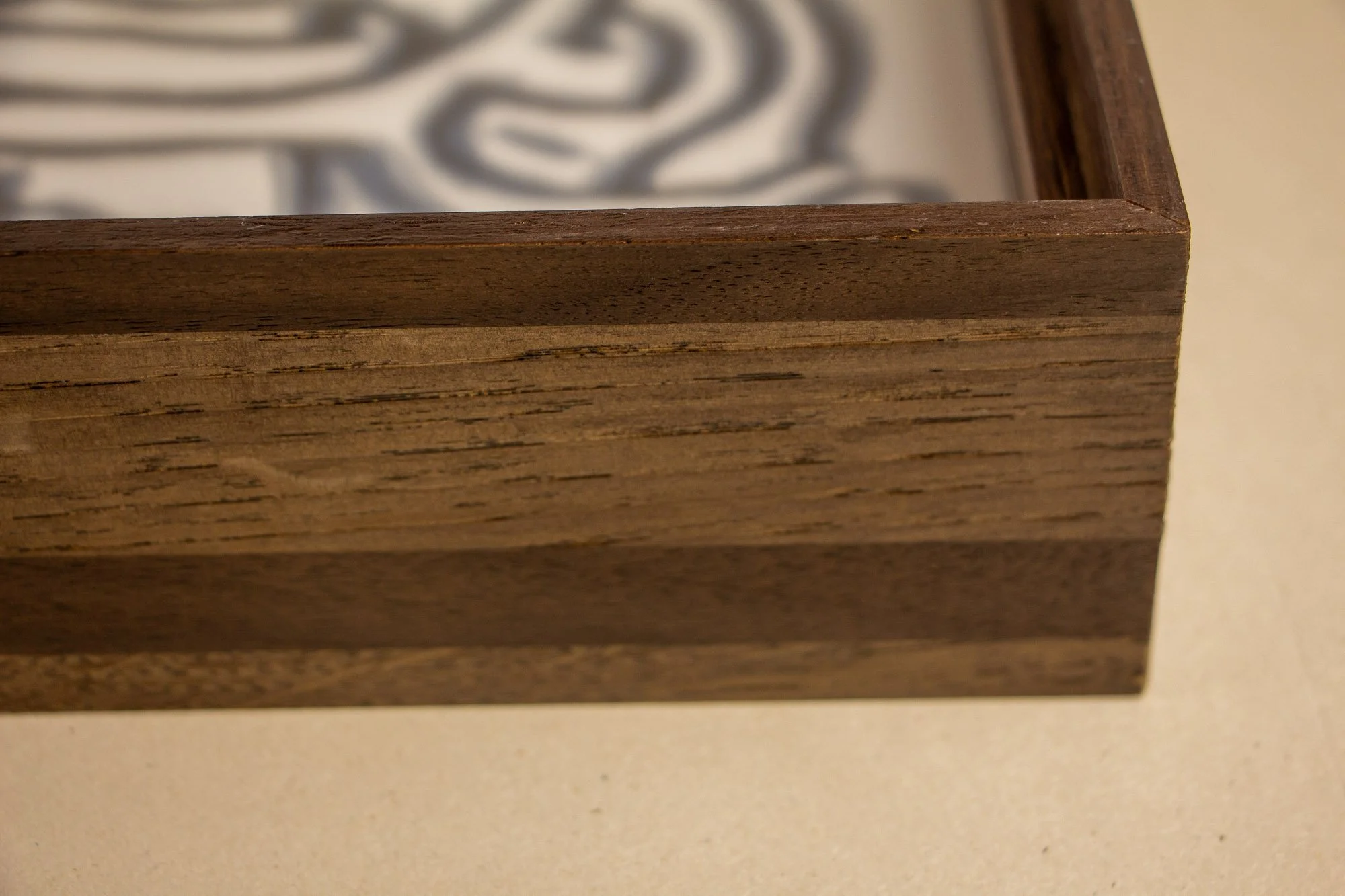 Luminous Parallax 003 frame: front corner detail with the artwork softly receding behind glass, showing the precise mitred joint and the warm, figured inner lip set within the darker outer frame.