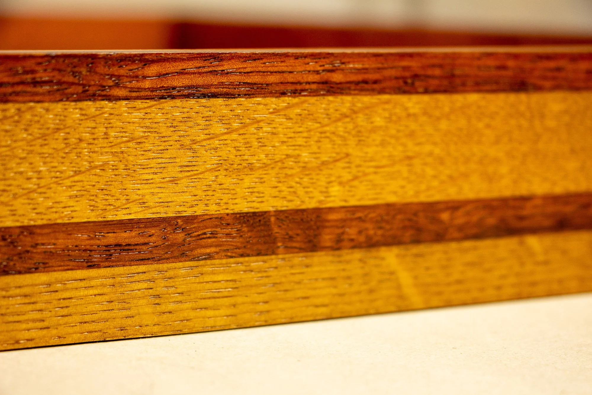 Unseen Signifiers 004 frame detail: side-profile close-up of the layered frame, showing a dark reddish top band, broad honey-toned middle band, and narrower reddish strip running horizontally through the centre. mahogany, oak and beech wood.