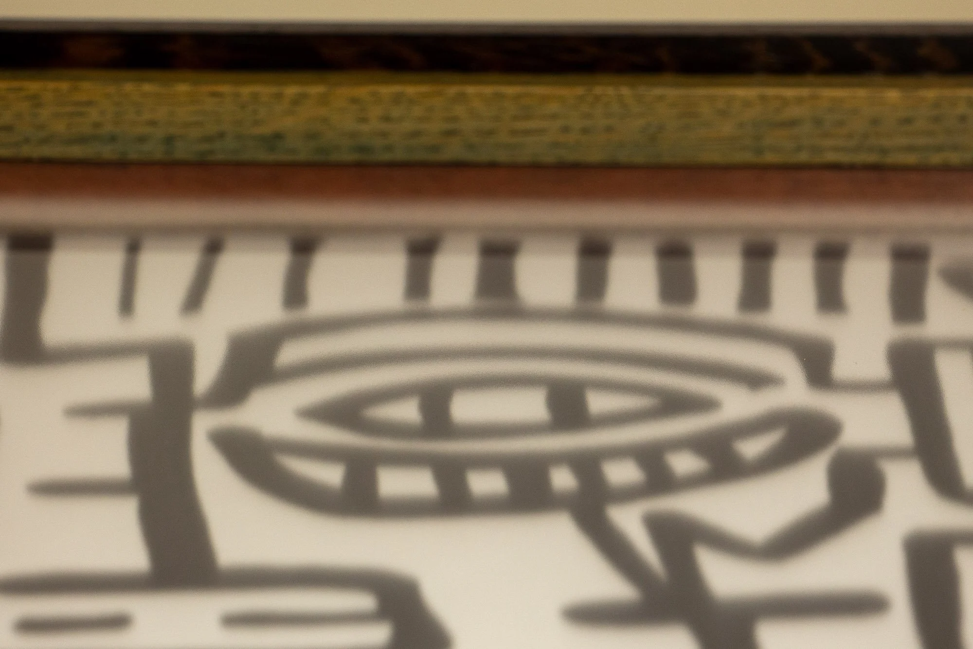 Elusive Cocoon 004 frame: upper-edge detail with a dark wengé outer rail, olive-toned inner band, and orange inner lip above a softly focused eye motif in the drawing below.