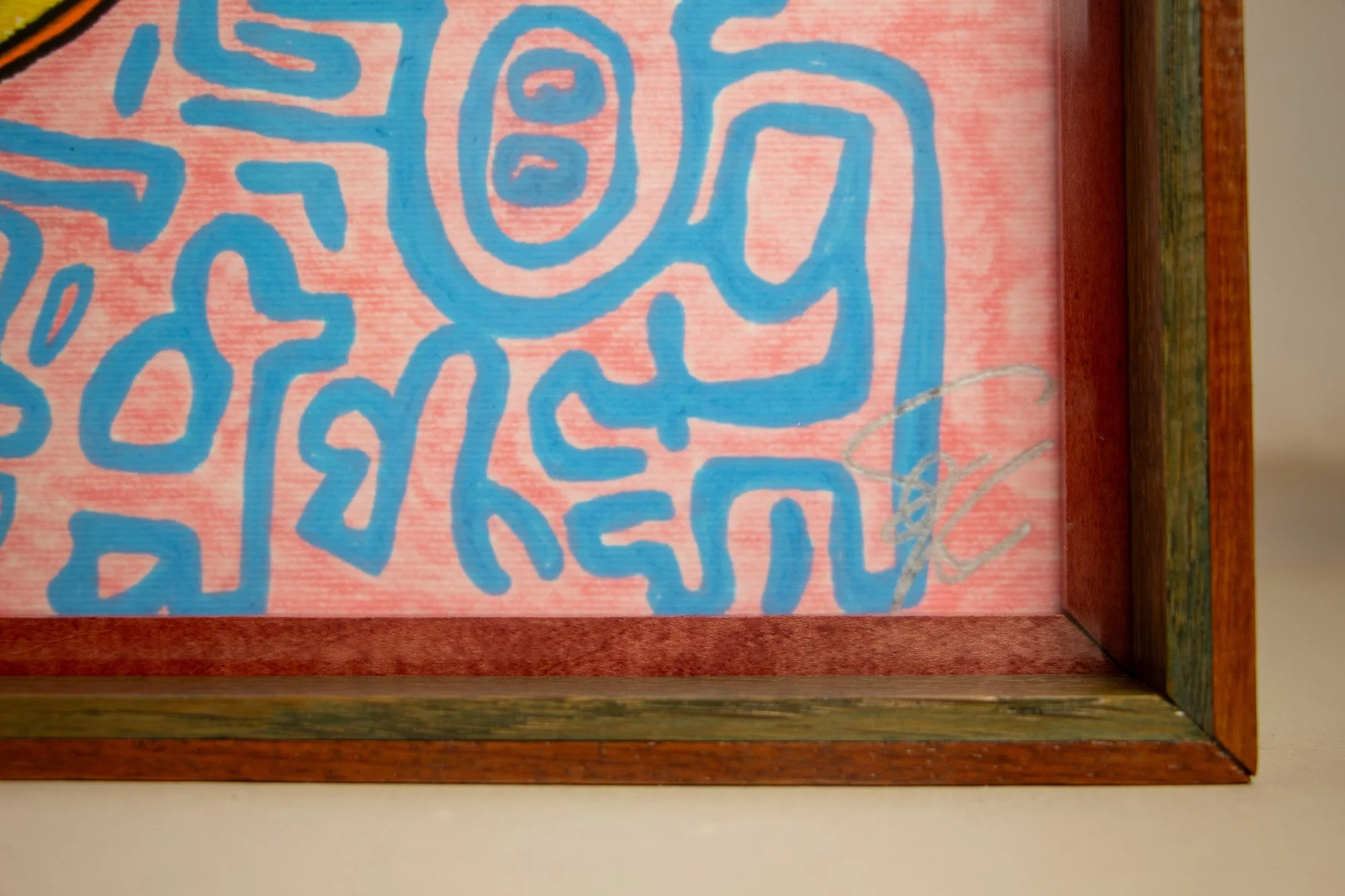 Unseen Signifiers 006 frame detail: lower-right corner view of the frame showing the olive-green inner liner, reddish-brown outer rim, and the silver signature visible on the artwork behind the glass. mahogany, oak and beech wood.