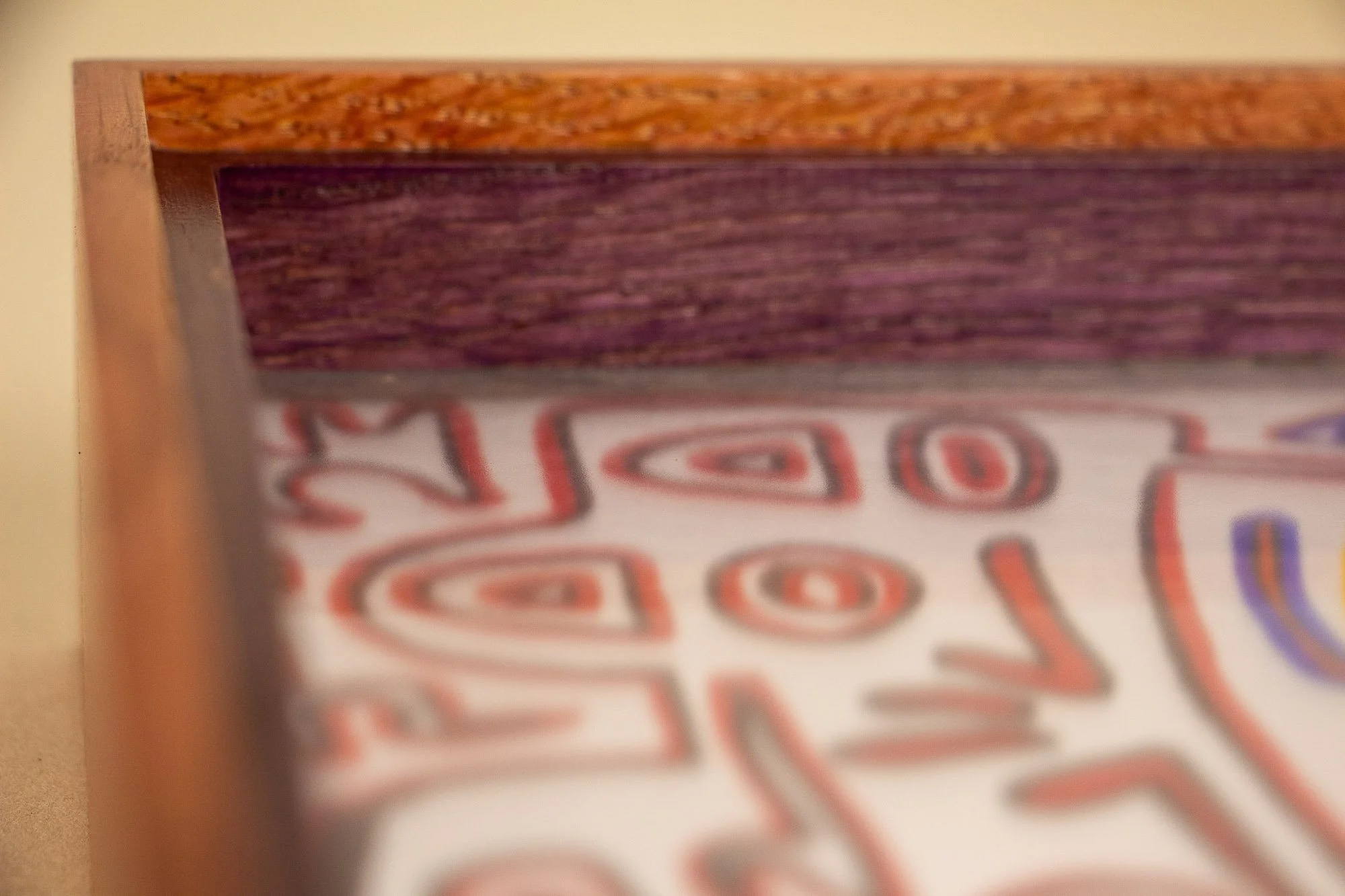 Eclipsing Gravitas 003 frame: corner detail from above, revealing the warm pink-orange outer frame, a purple-toned inner lip, the clean miter joinery, and the artwork softly visible beneath the glass.