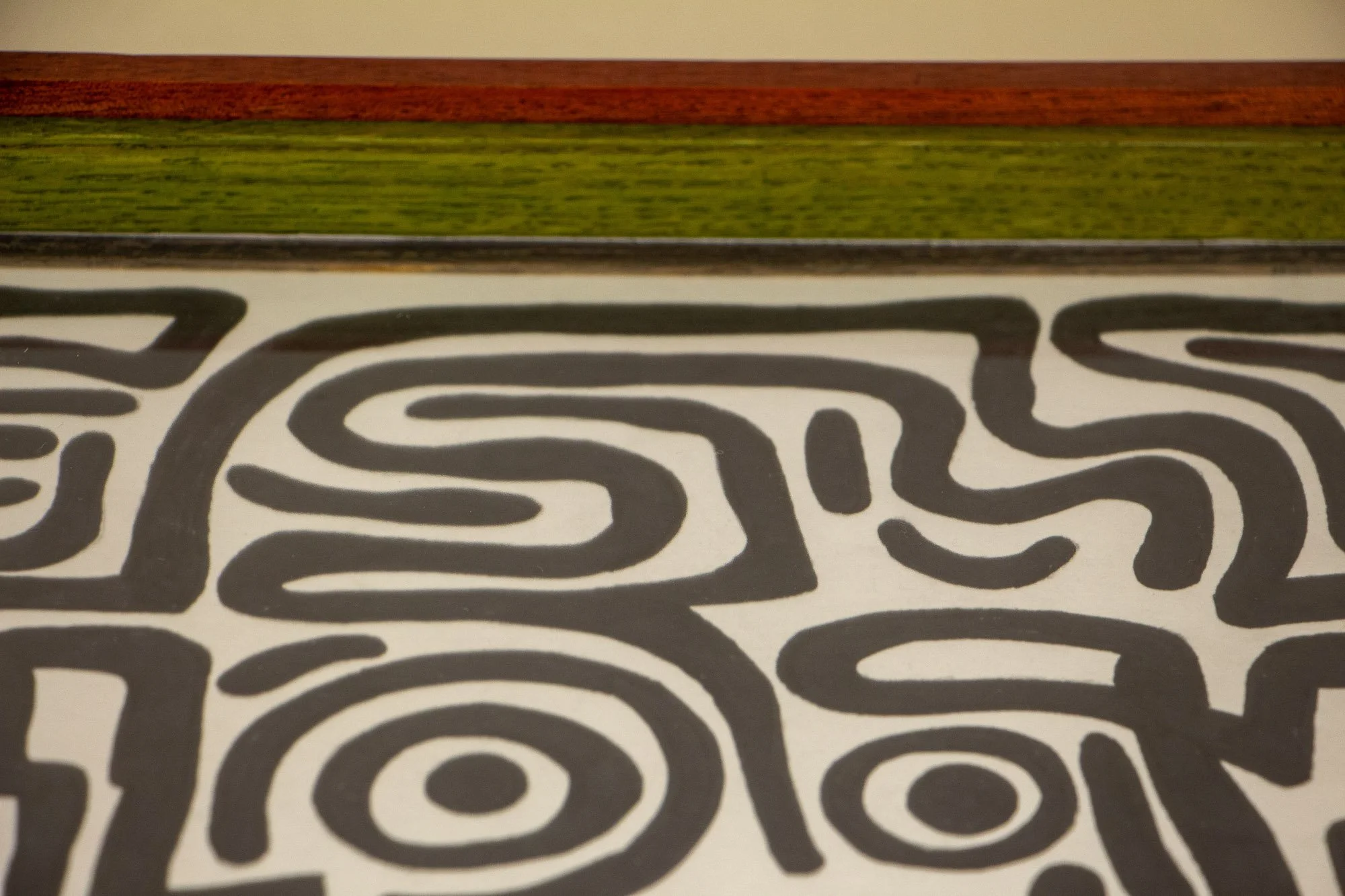 Resonant Syntax 003 frame: upper inside corner detail of the frame, showing the red outer edge, green inner band, granada-toned inner lip, and the artwork beneath the glass