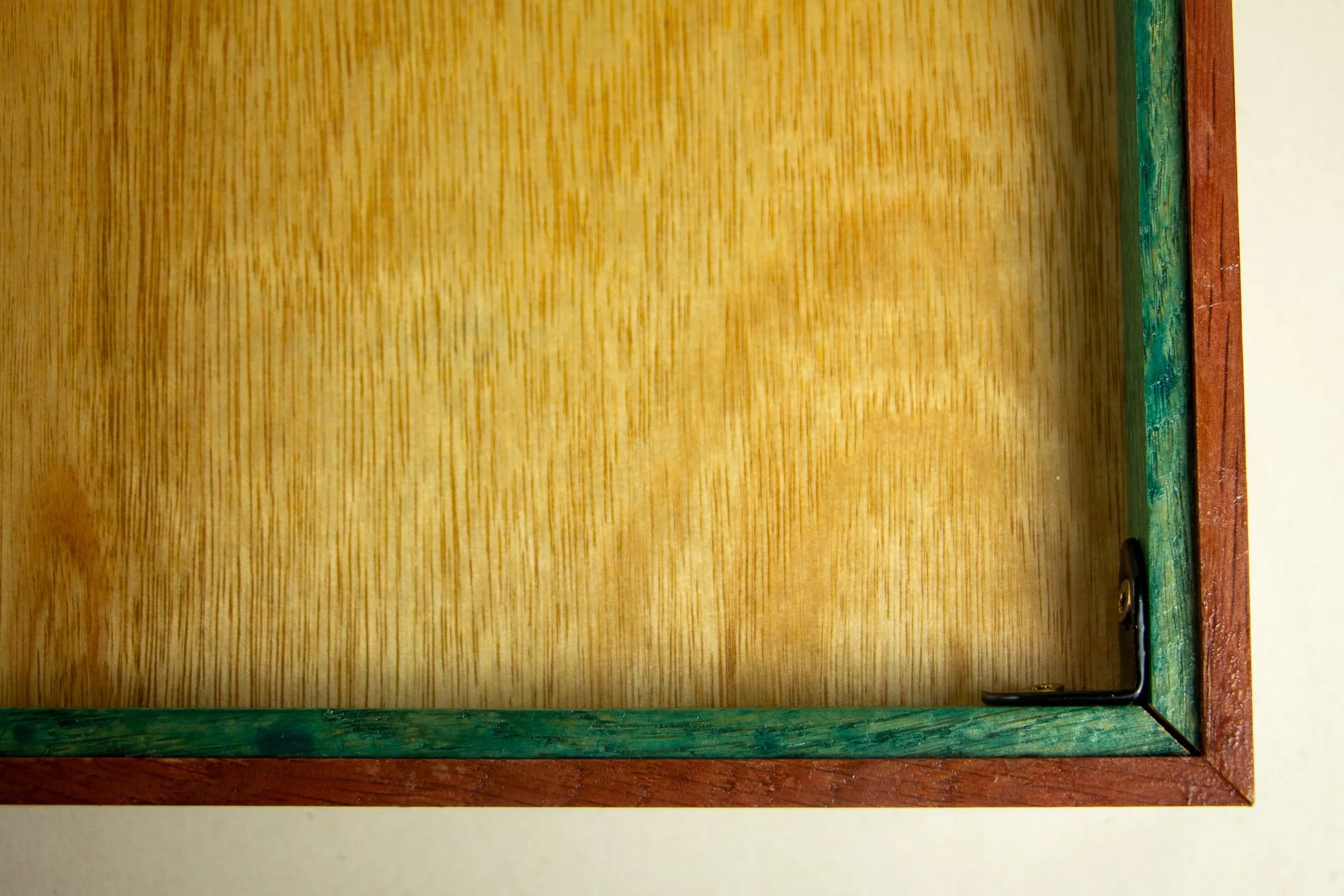 Unseen Signifiers 010 frame detail: rear corner close-up showing the warm wood back panel, the green-painted inner frame edge, and the black corner bracket fixed into the mitered construction.