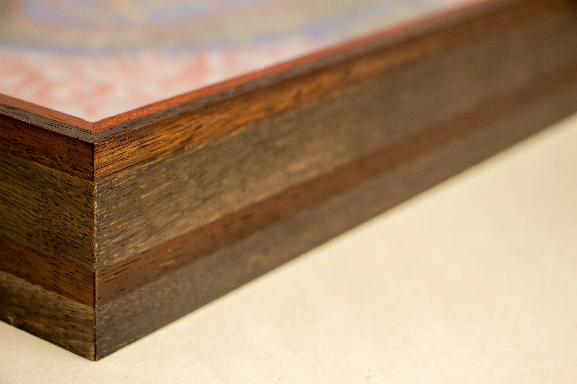 Unseen Signifiers 003 frame detail: angled side view of the frame showing its dark layered wood construction, with a warm reddish top edge and a darker central band running through the profile. mahogany, oak and beech wood.