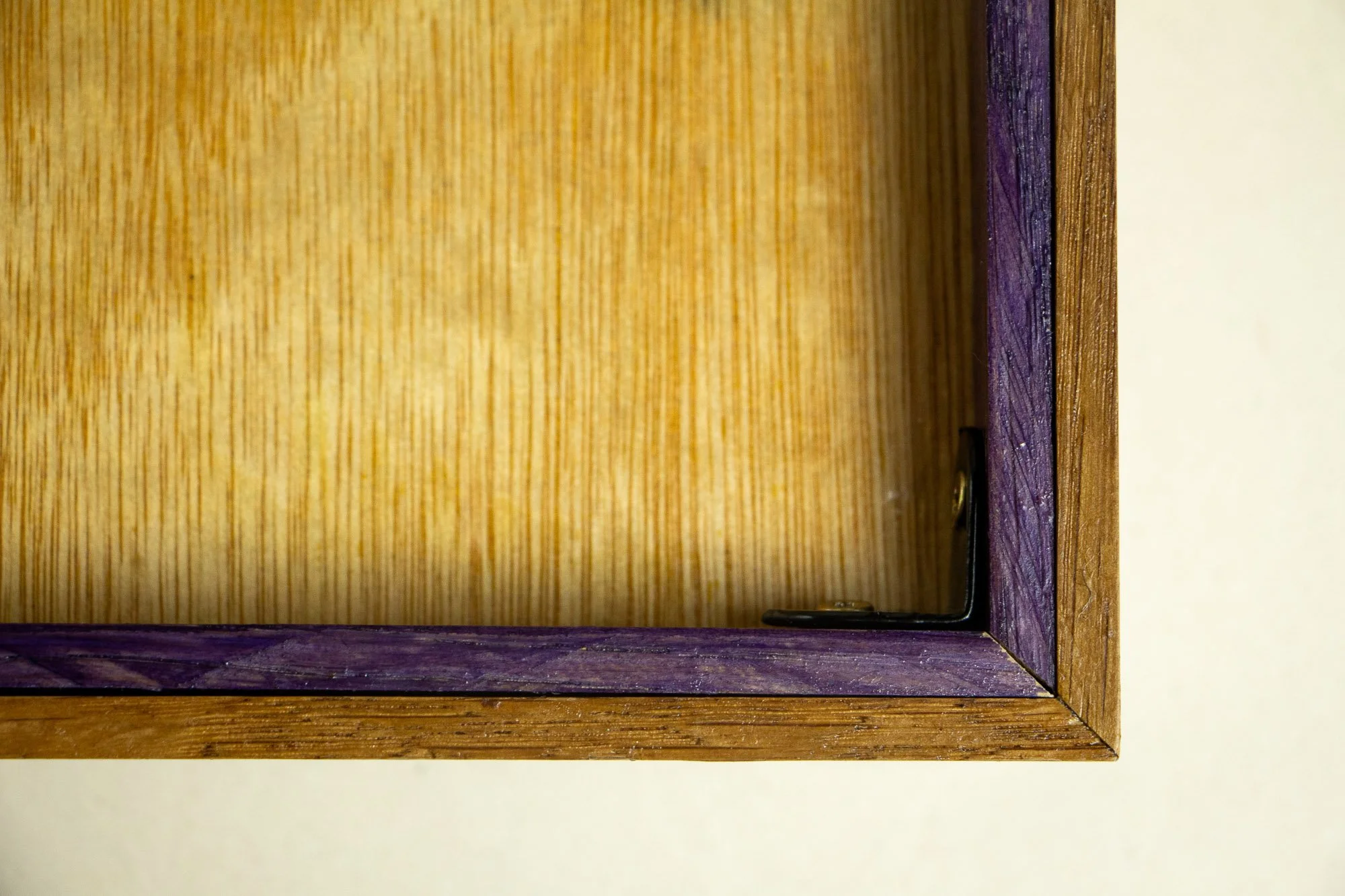 Unseen Signifiers 004 frame detail: reverse corner view of the frame, showing the plywood backing, black corner bracket, and purple-toned inner support against the layered wooden construction.