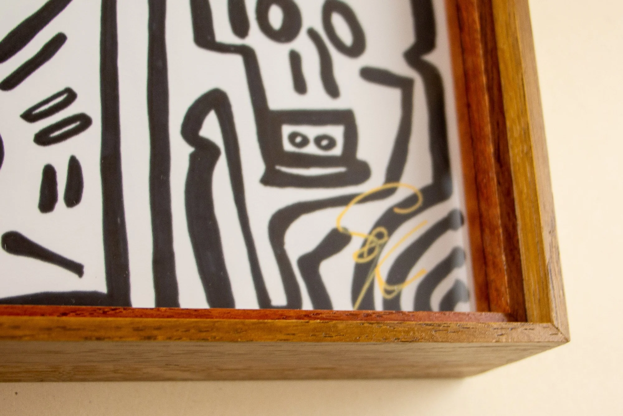 Veiled Alchemist 001 frame detail: corner view of the framed work, showing the golden signature on the drawing, the reddish inner edge, the warm outer wood, and the precise transition between artwork, glazing, and frame.