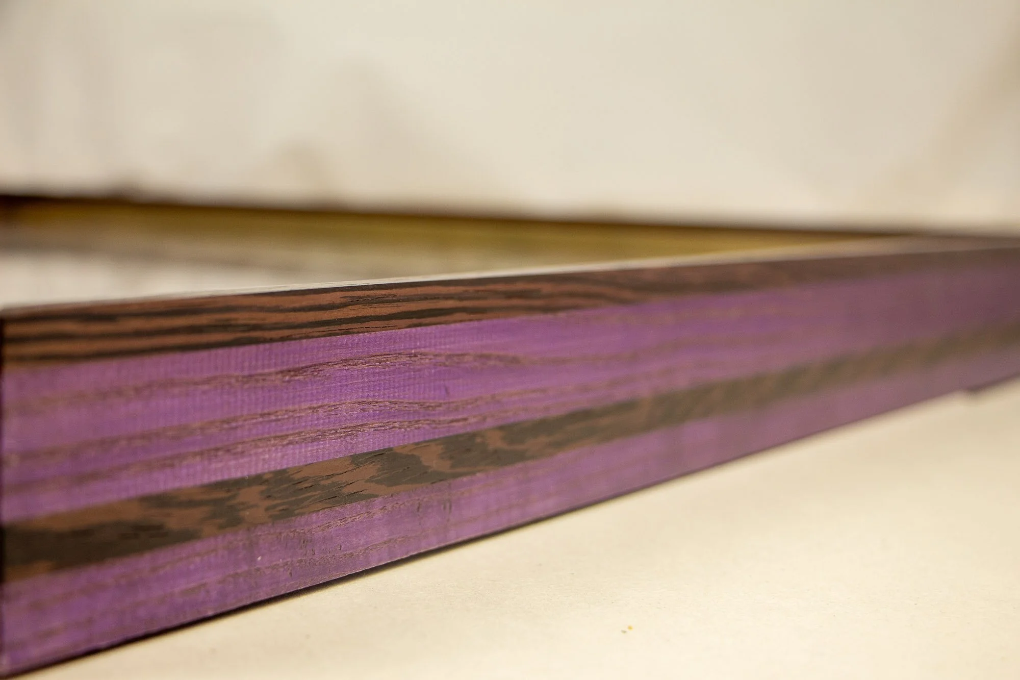 Elusive Cocoon 003 frame: angled side detail of the layered wengé-and-oak frame, showing violet-toned oak bands, darker wengé sections, visible grain, and a long shallow profile.