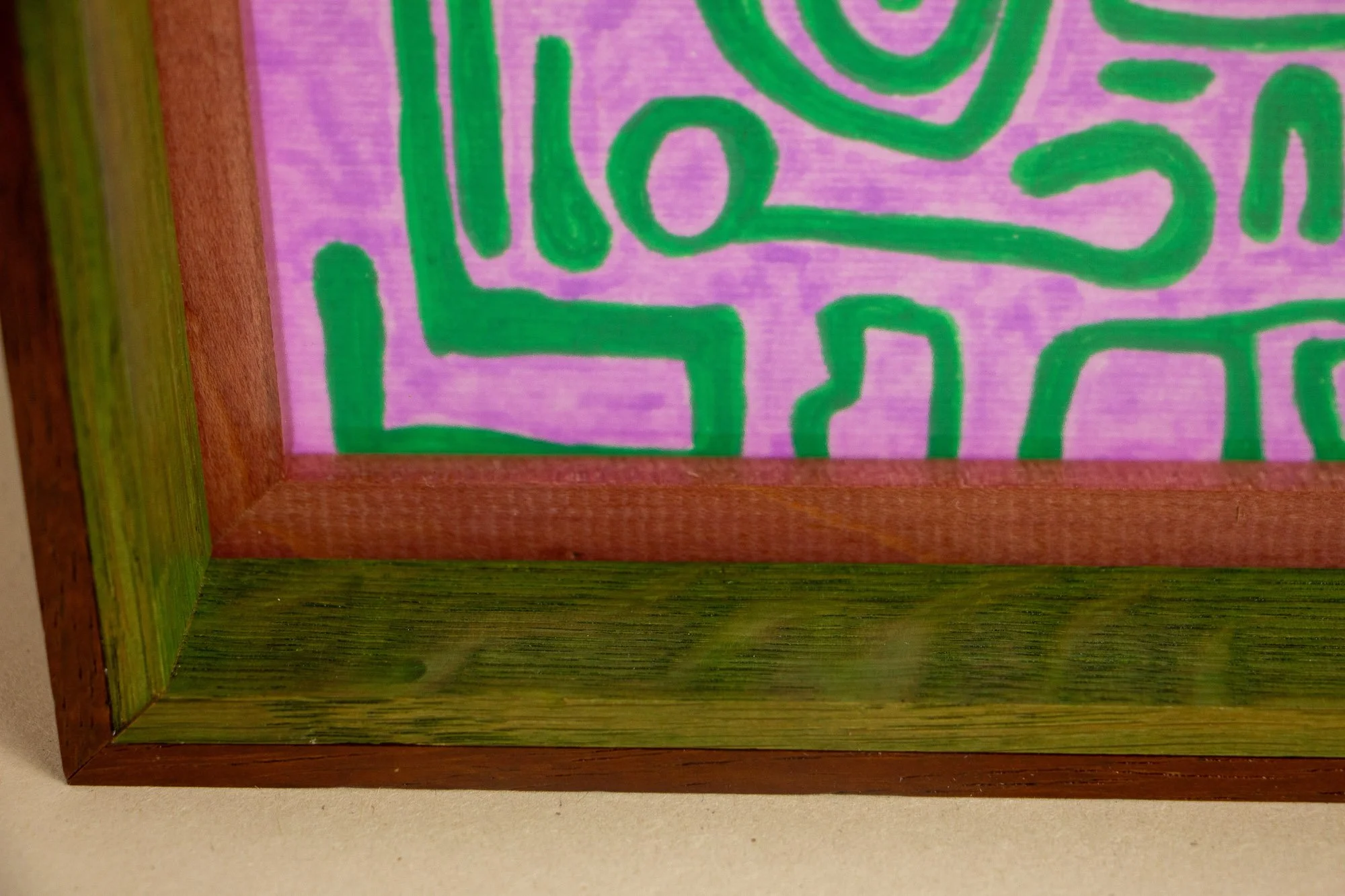 Unseen Signifiers 002 frame detail: lower-left corner of the framed work, where the lilac ground and green signs meet the reddish inner spacer and green-stained inner band of the frame. mahogany, oak and beech wood.