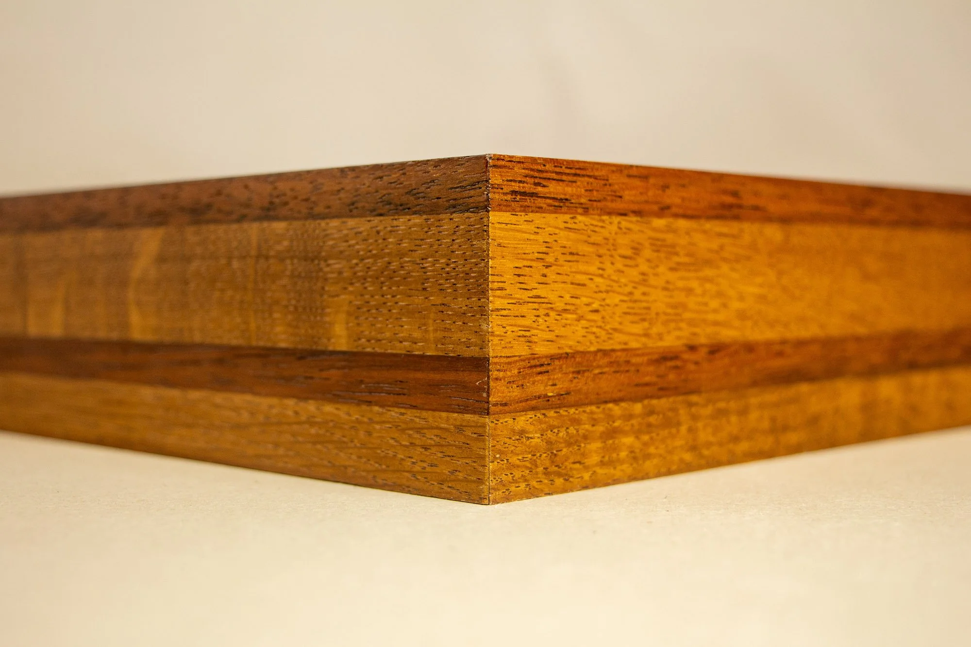 Unseen Signifiers 008 frame detail: angled corner view of the deep frame profile, showing the layered wood construction with alternating warm golden-brown and darker brown bands. mahogany, oak and beech wood.