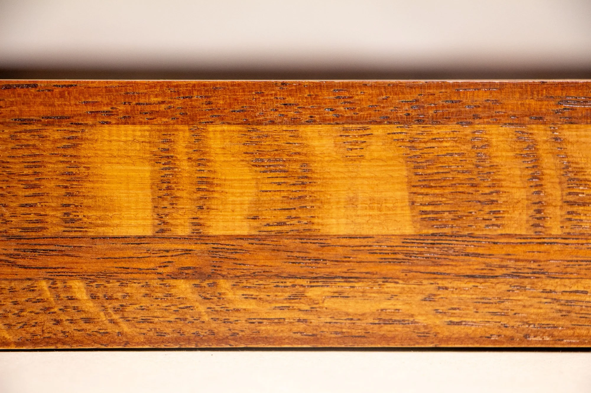 Turbulent Aegis 001 frame detail: close-up of the handcrafted frame surface, showing the warm amber wood grain, tonal layering, and subtle reflective finish.