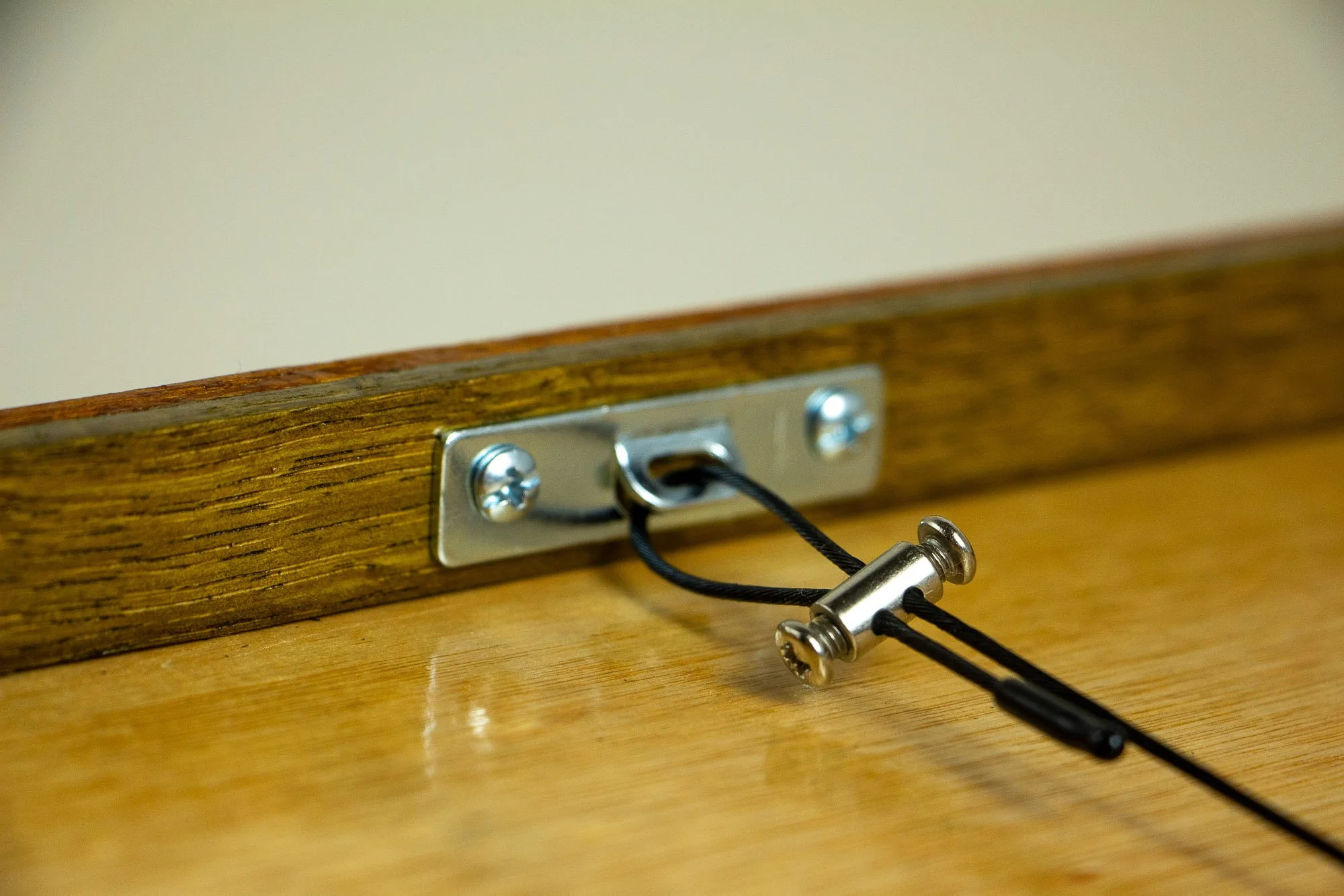Unseen Signifiers 006 frame detail: close-up of the rear hanging system with metal plate, black hanging cord, and adjustable metal fastener mounted against the wooden back panel.