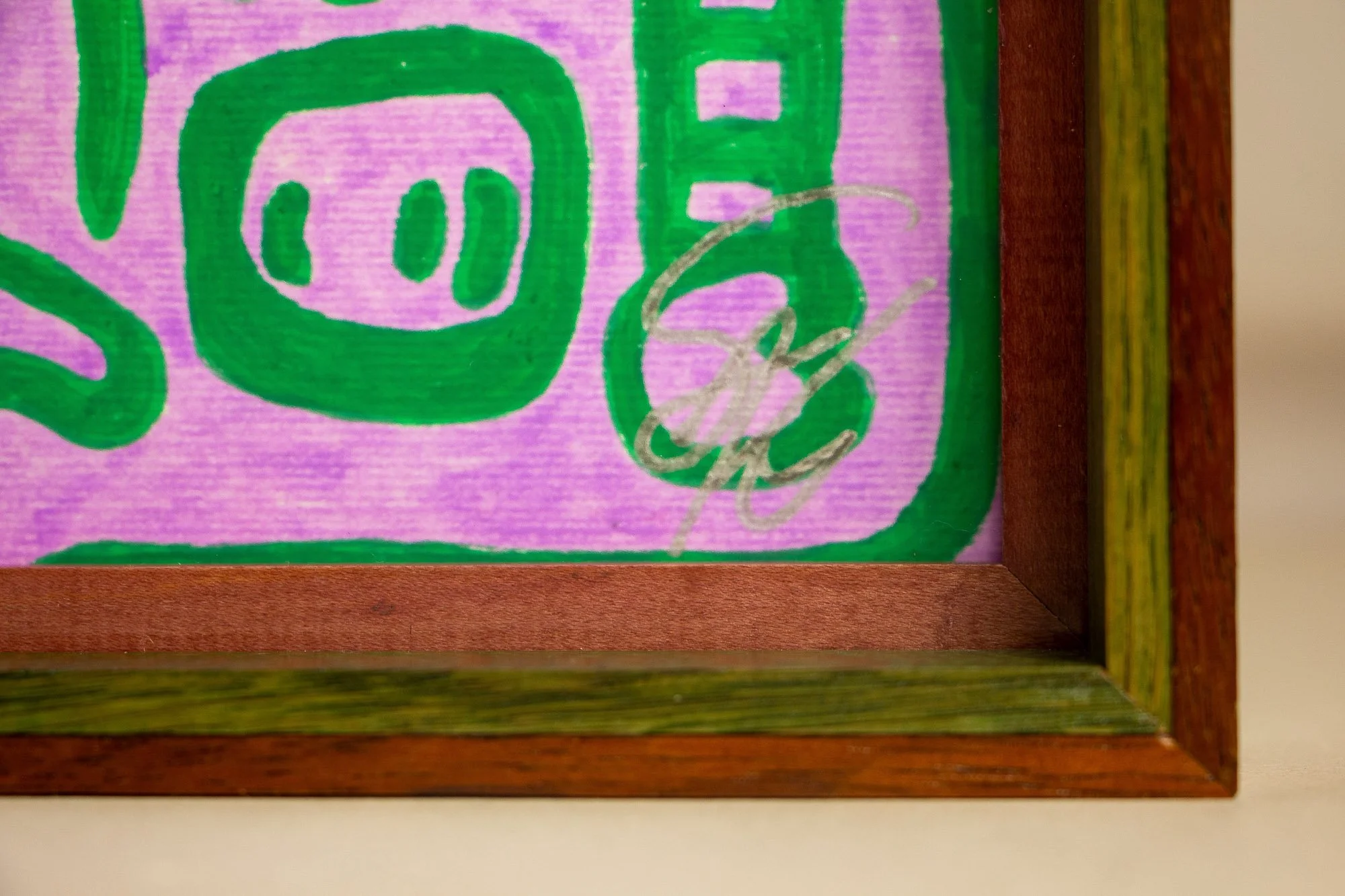 Unseen Signifiers 002 frame detail: lower-right corner of the framed work with the silver signature visible on the lilac ground, bordered by the reddish inner spacer and green-toned frame band. mahogany, oak and beech wood.