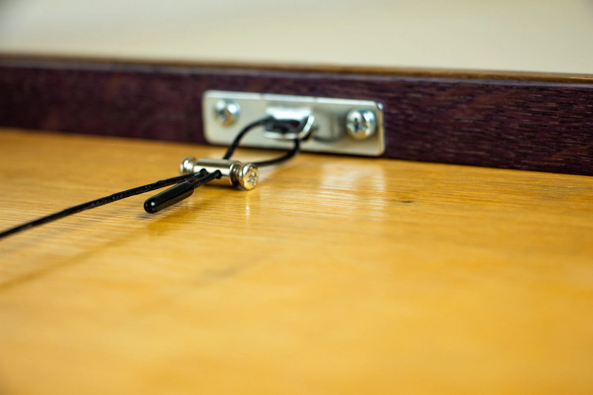 Unseen Signifiers 004 frame detail: reverse close-up of the wall-hanging hardware, showing the metal fixing plate, black cable loop, and tension fastener mounted against the plywood back.