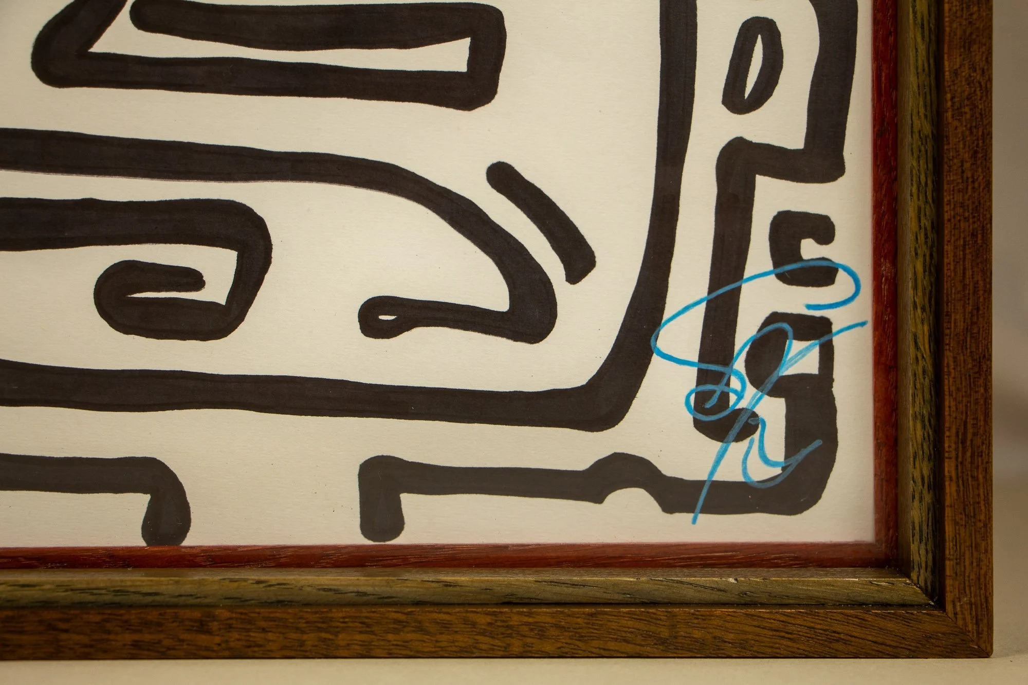 Resonant Syntax 002 frame: lower-right corner detail showing the blue signature on paper, bordered by the layered mahogany-and-oak frame in a mint, blue, and pink sequence