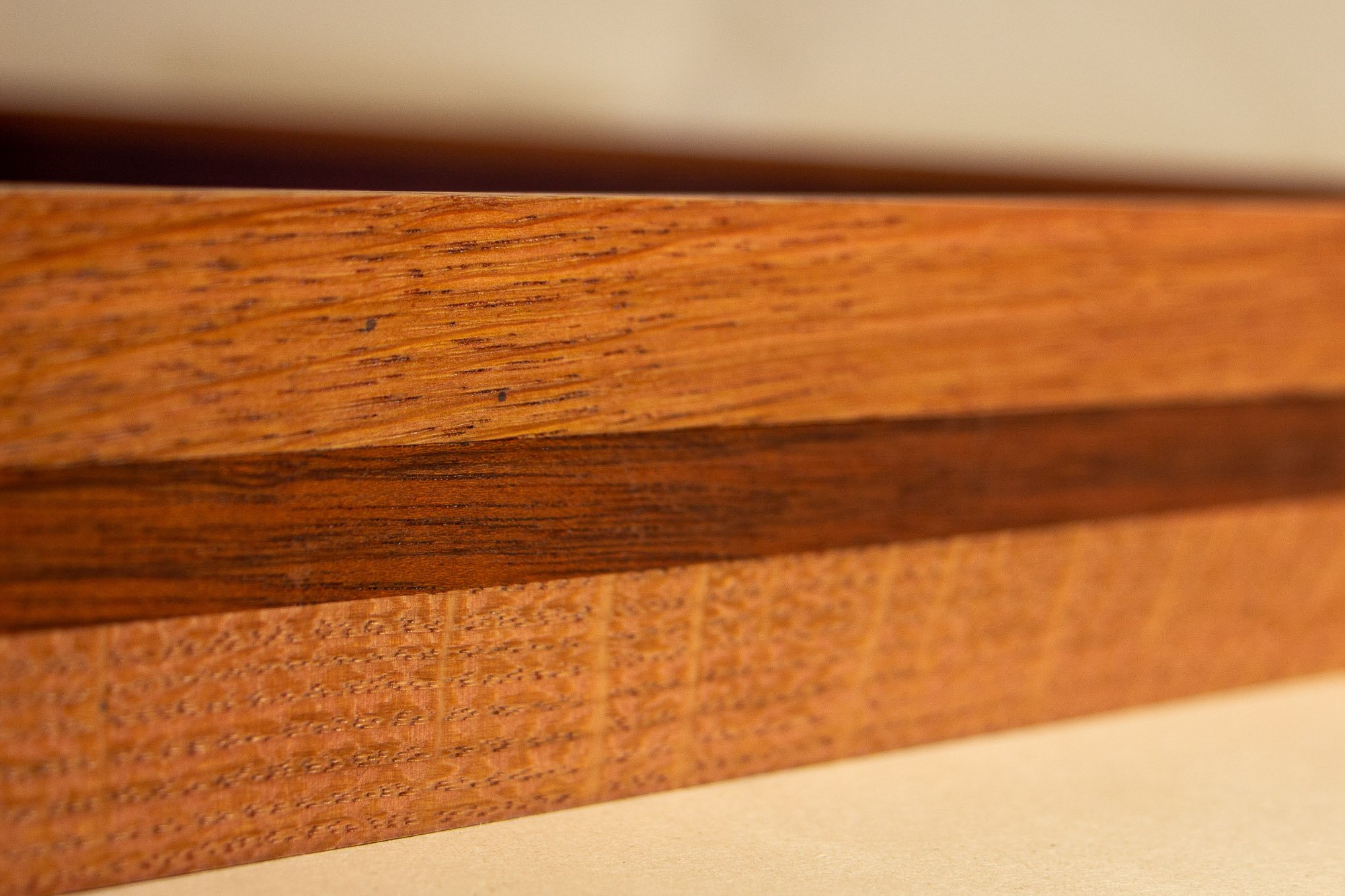 Eclipsing Gravitas 003 frame: macro side view of the frame profile, highlighting the smooth oak grain, the darker mahogany band running through the middle, and the crisp linear edge of the glazing above.