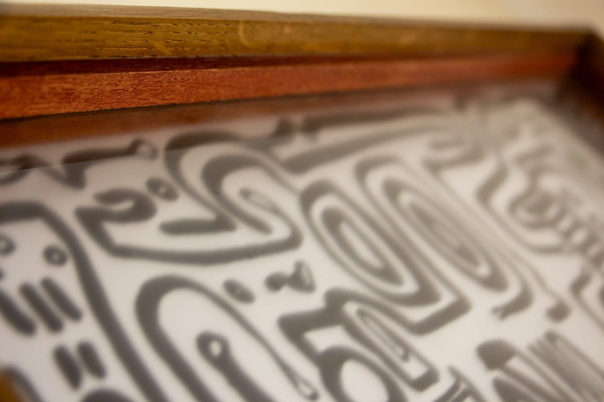 Veiled Alchemist 001 frame detail: angled view across the top inner frame edge, highlighting the warm elm tone, the red-toned inner band, and the way the layered profile softly guides the eye toward the drawing.